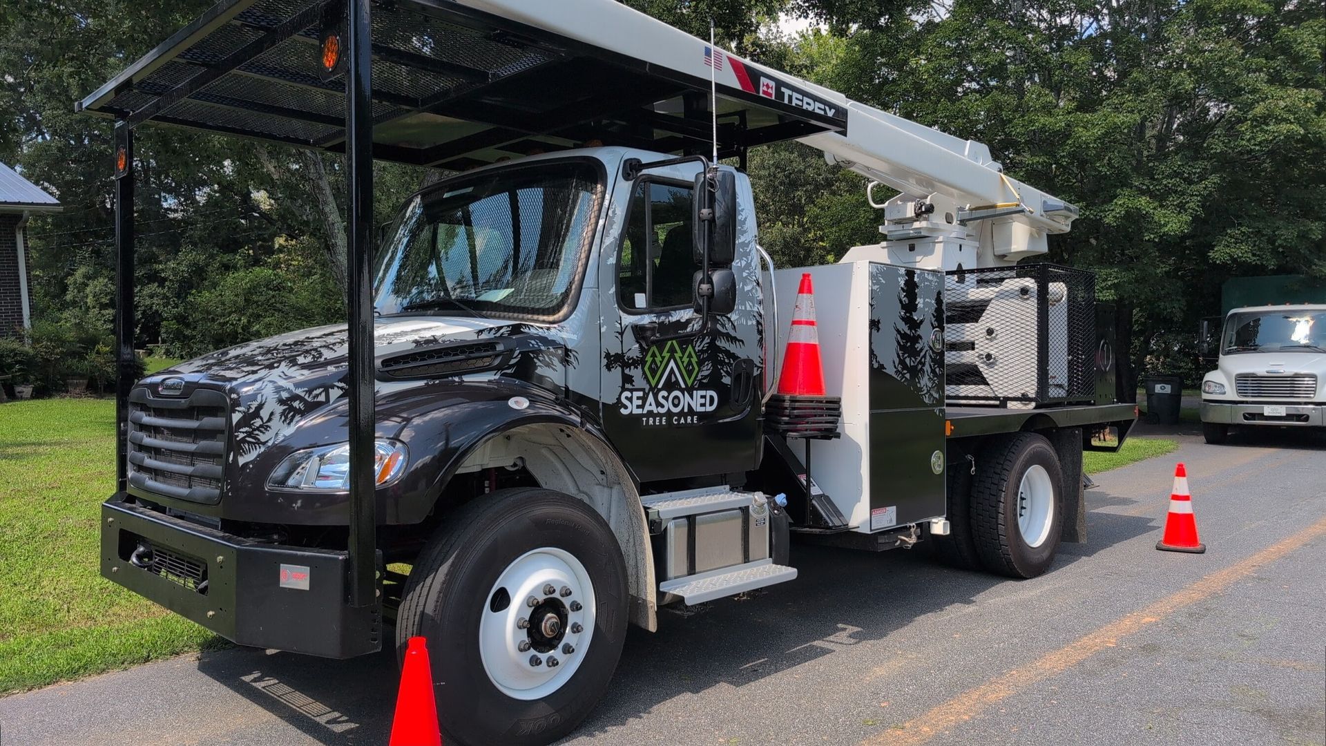 Black utility truck with canopy parked roadside, surrounded by orange traffic cones