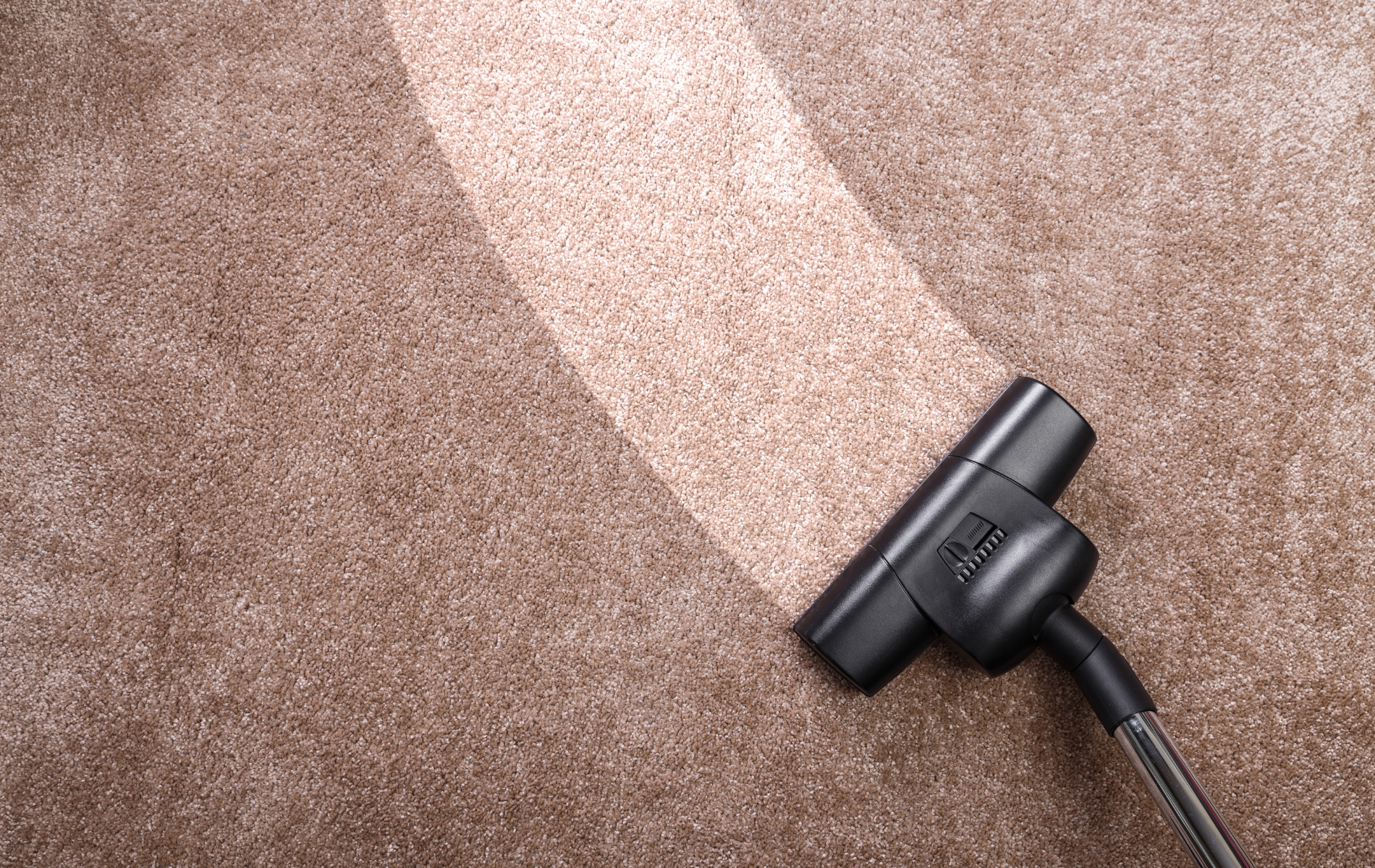 A vacuum cleaner attachment creates a clean, light-colored path across a textured, dark beige carpet.