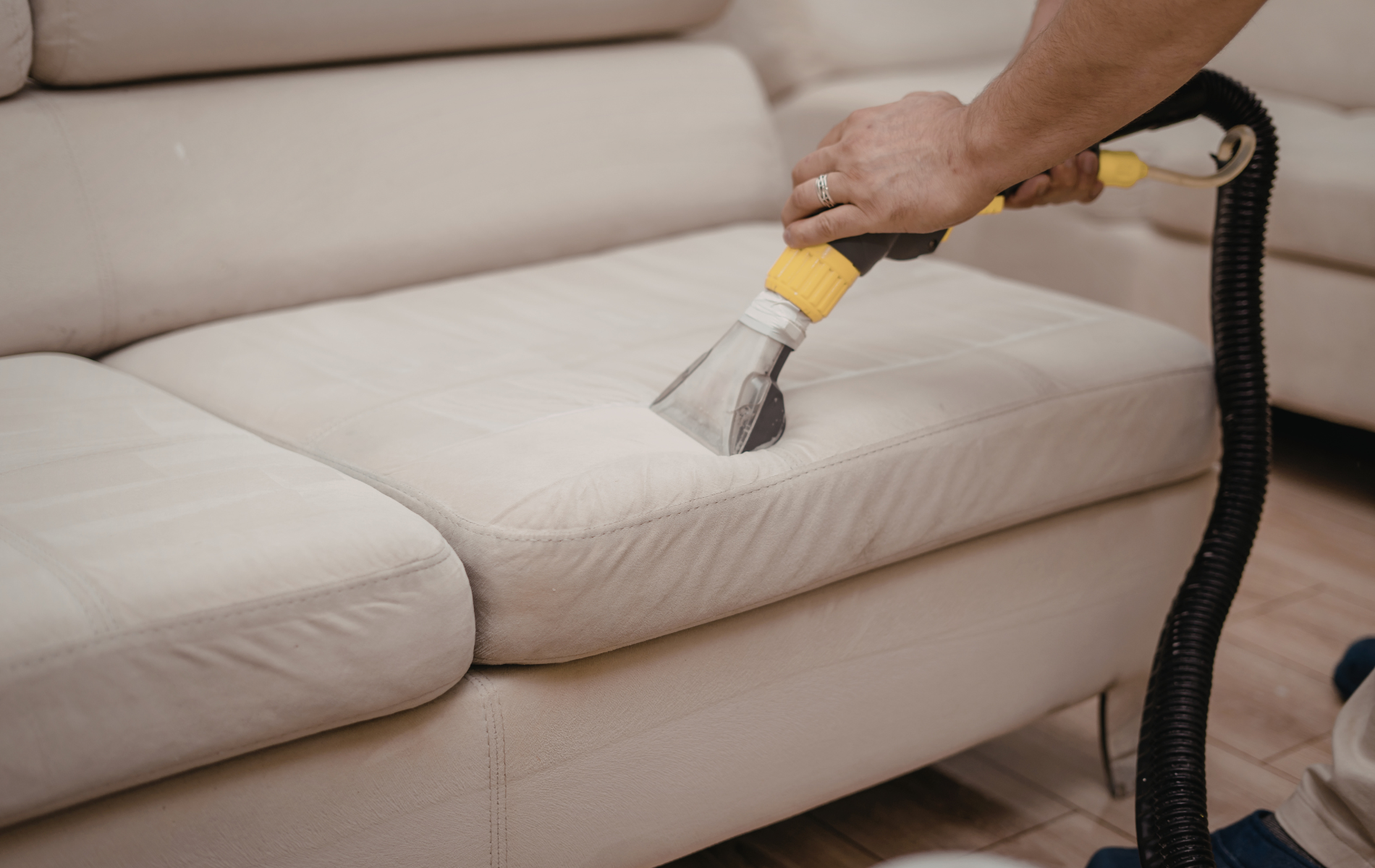 A person uses an upholstery cleaning machine to clean a light-colored fabric sofa.