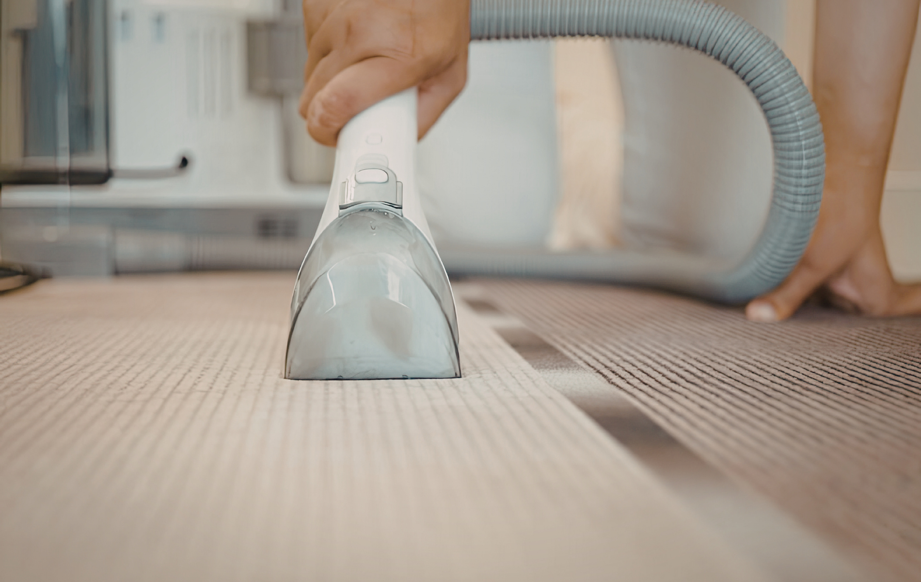 A person uses a handheld machine to clean a carpet, showing a clear contrast between the cleaned and uncleaned sections.
