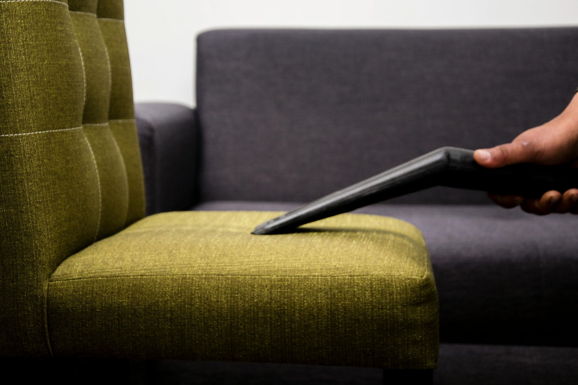 A person uses a handheld upholstery cleaning tool to deep clean a light-colored fabric sofa.