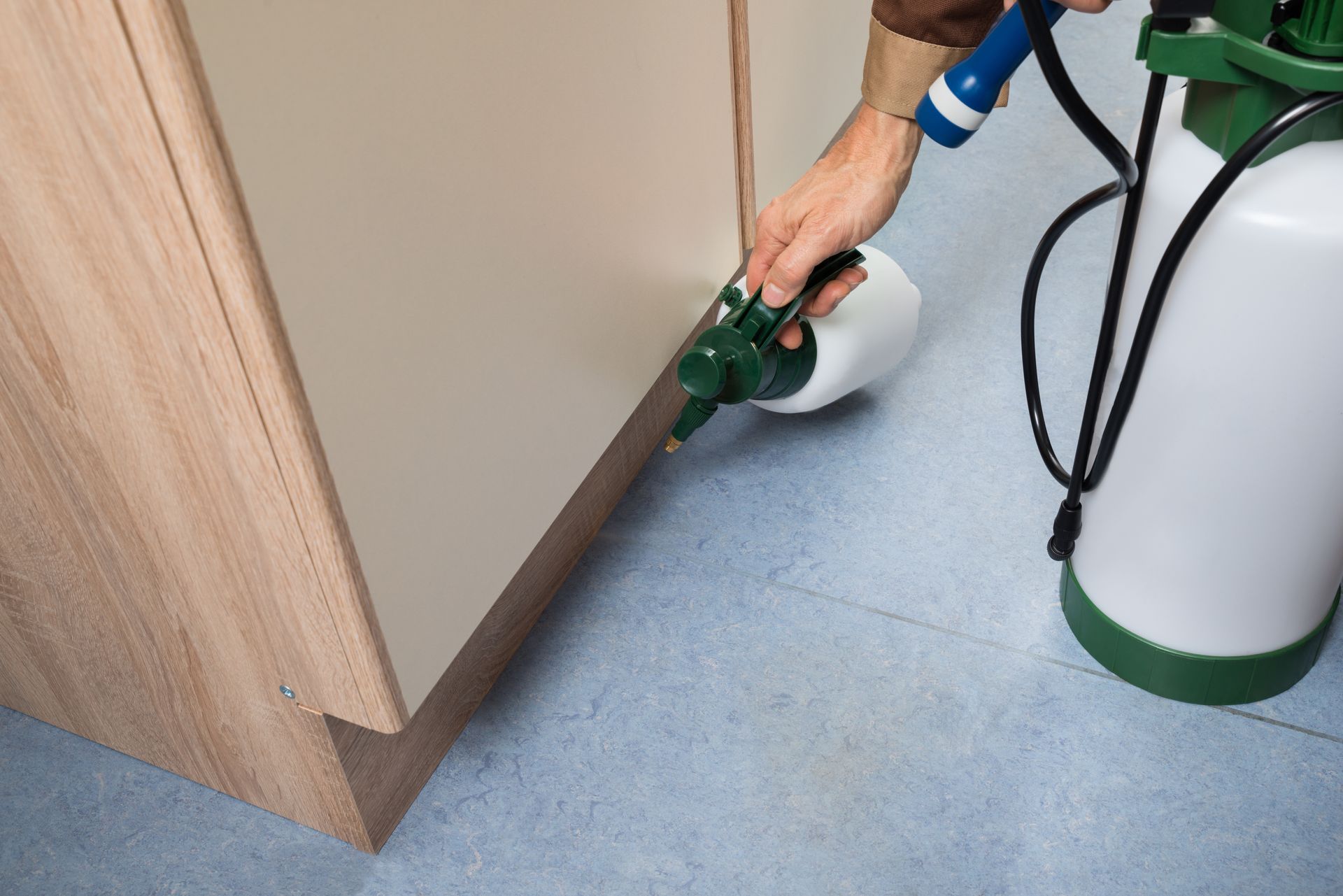 Person using a green floor-cleaning device next to a cabinet in a room with a blue floor