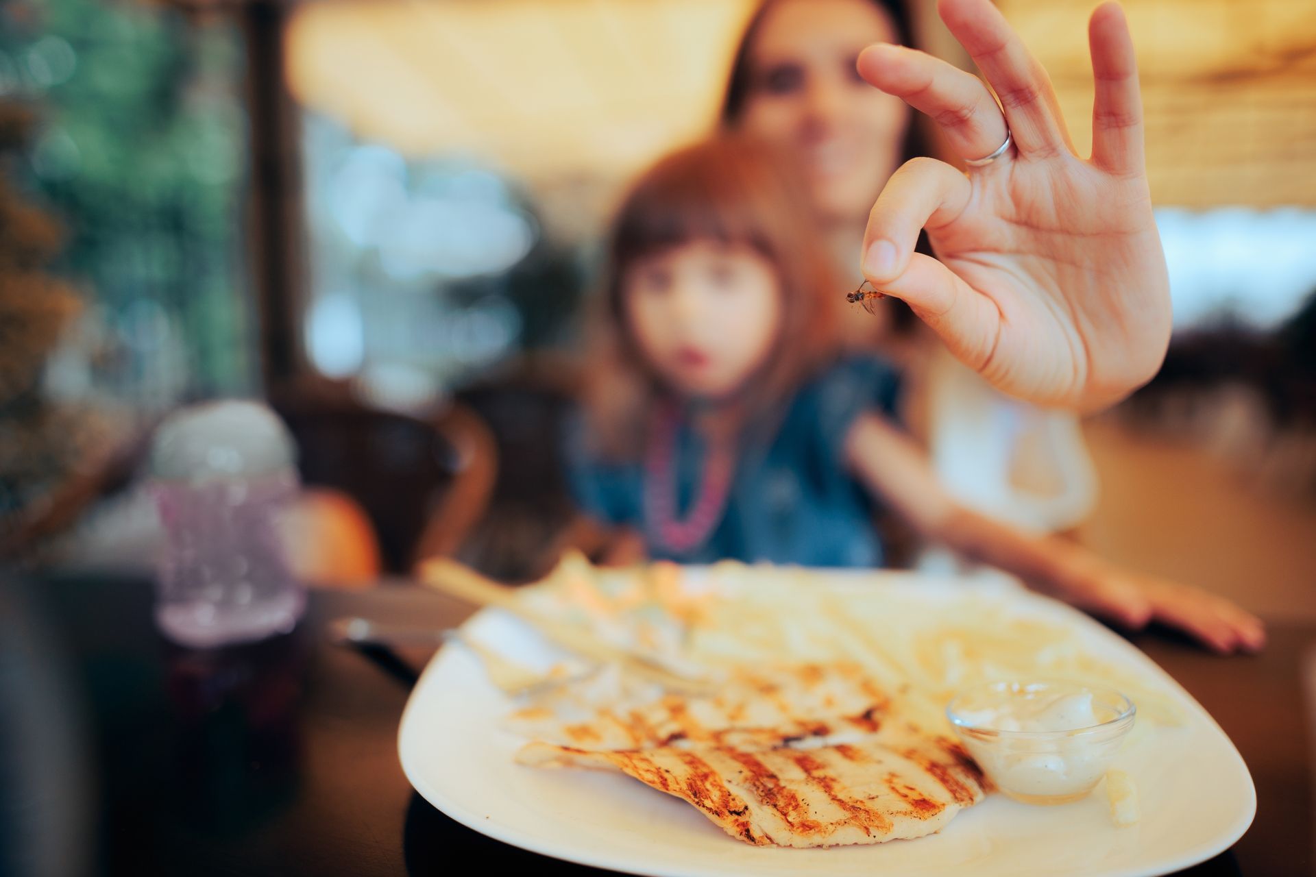Woman and child at a table, woman holding food up, smiling, plate of food visible, in a restaurant.