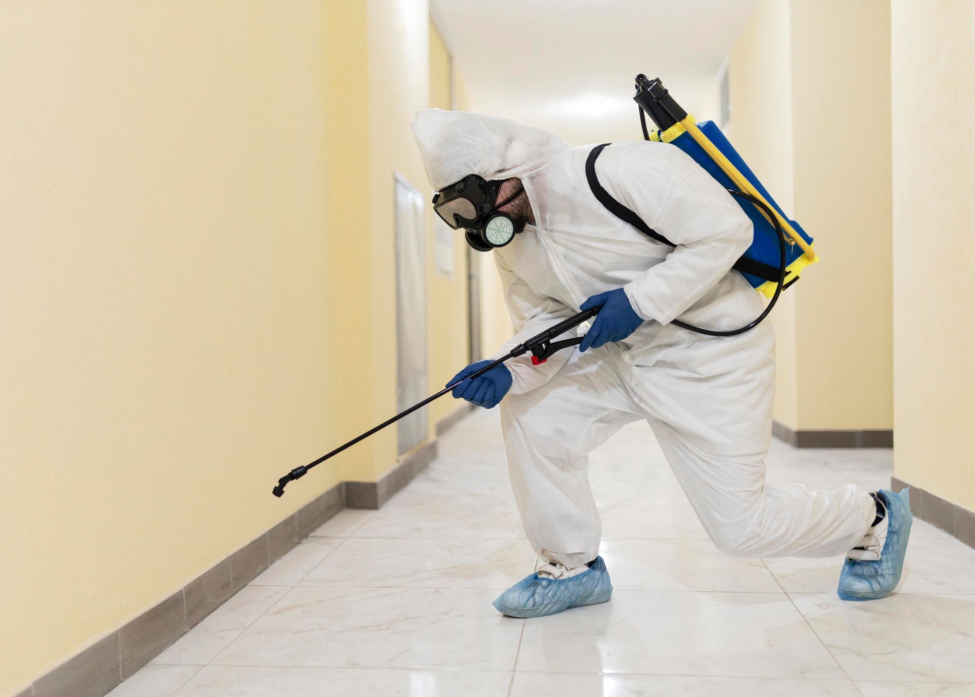 A man in a protective suit is spraying a hallway with a sprayer.