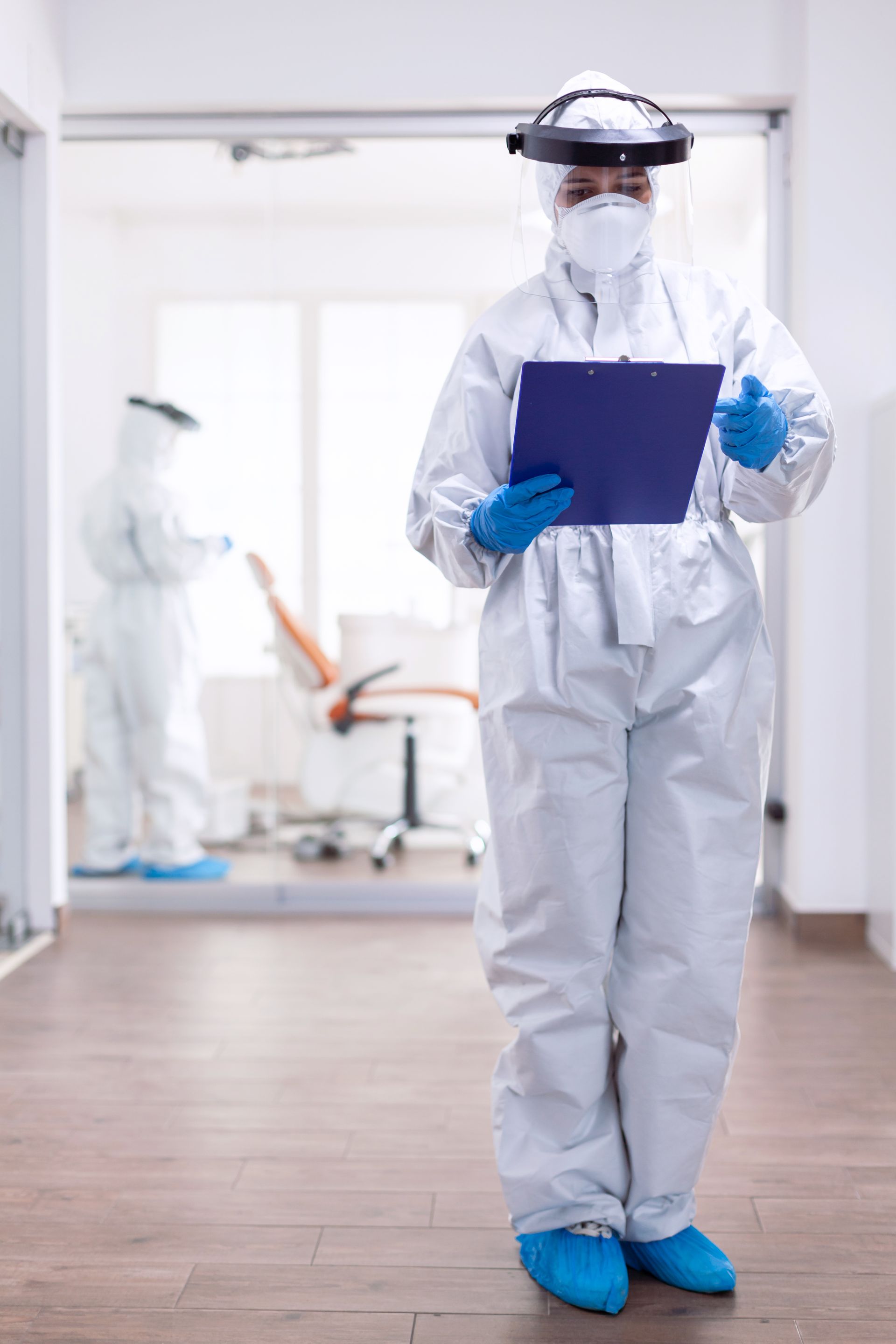 A nurse in a protective suit is holding a clipboard in a hospital.