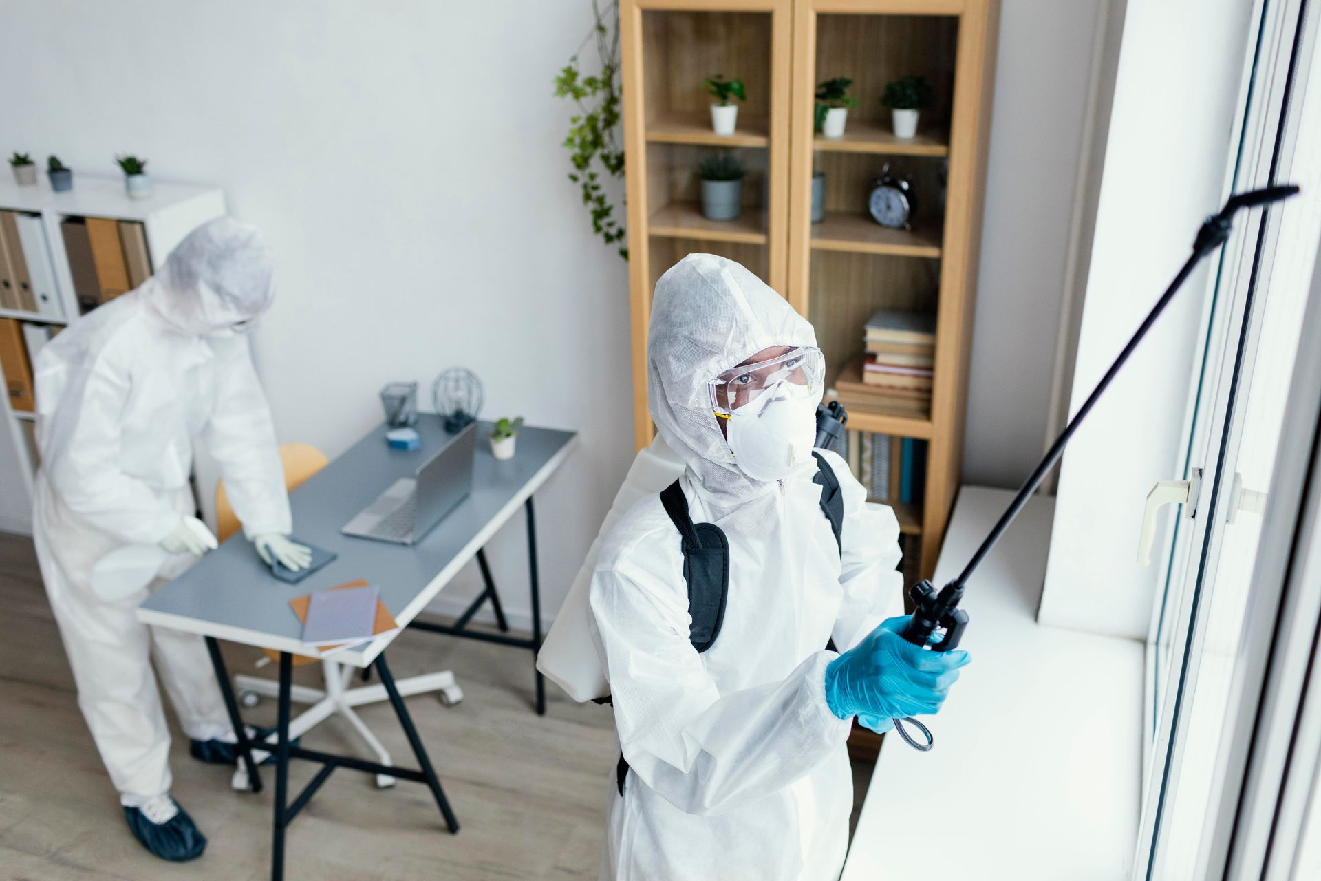 A man in a protective suit is spraying a room with a sprayer.