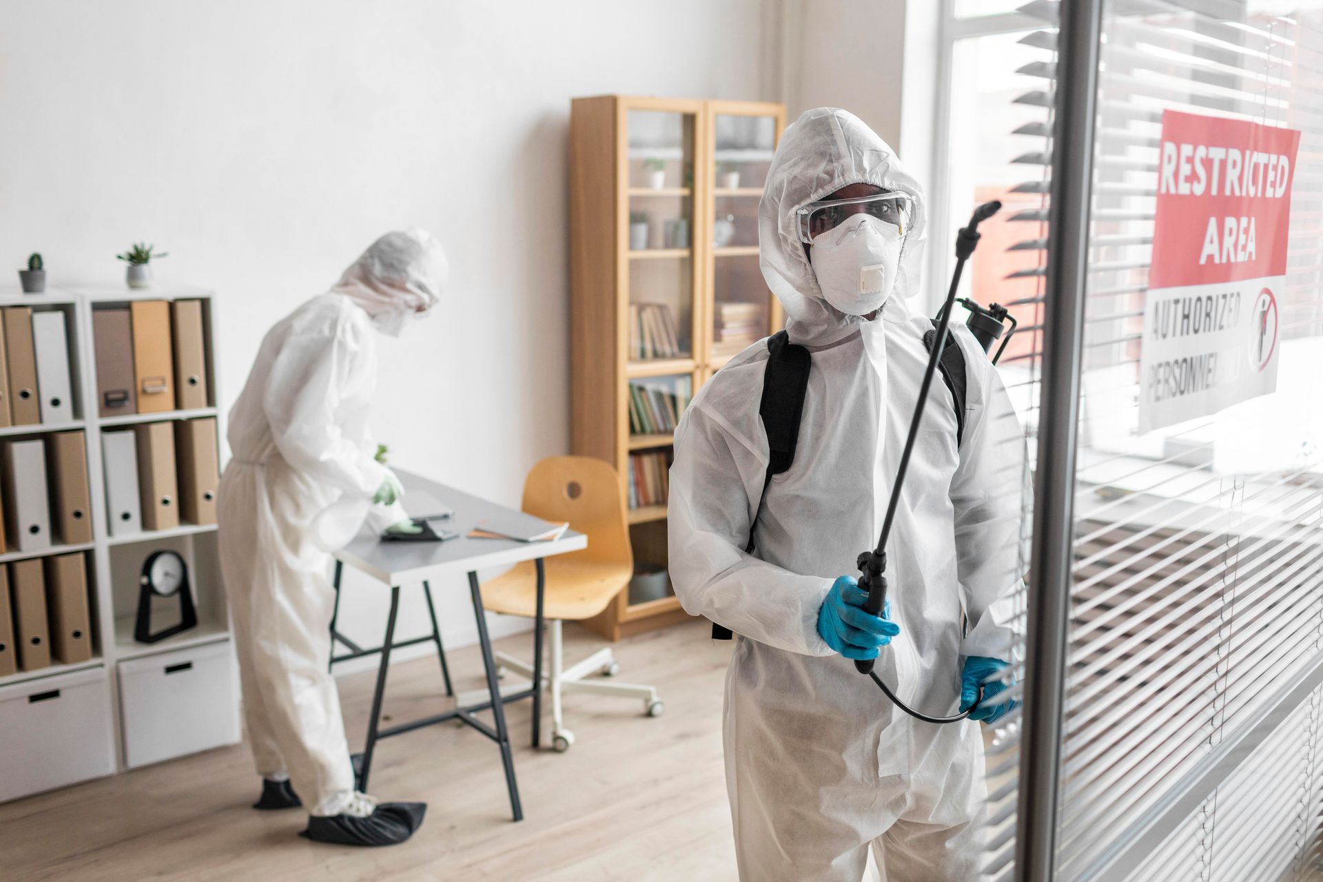A man in a protective suit is spraying a room with a sprayer.