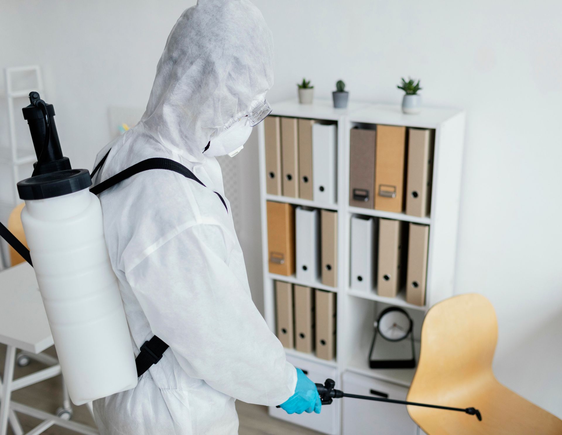 A man in a protective suit is spraying a room with a sprayer.