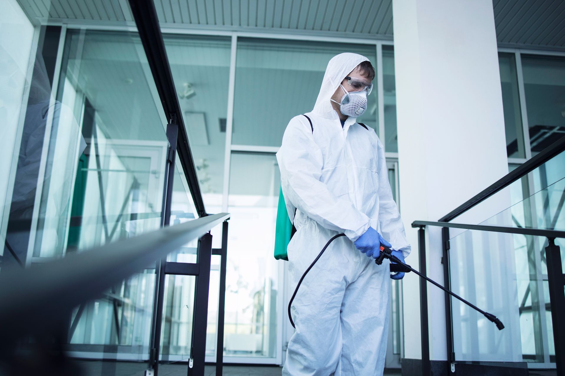A man in a protective suit and mask is spraying a building with a sprayer.
