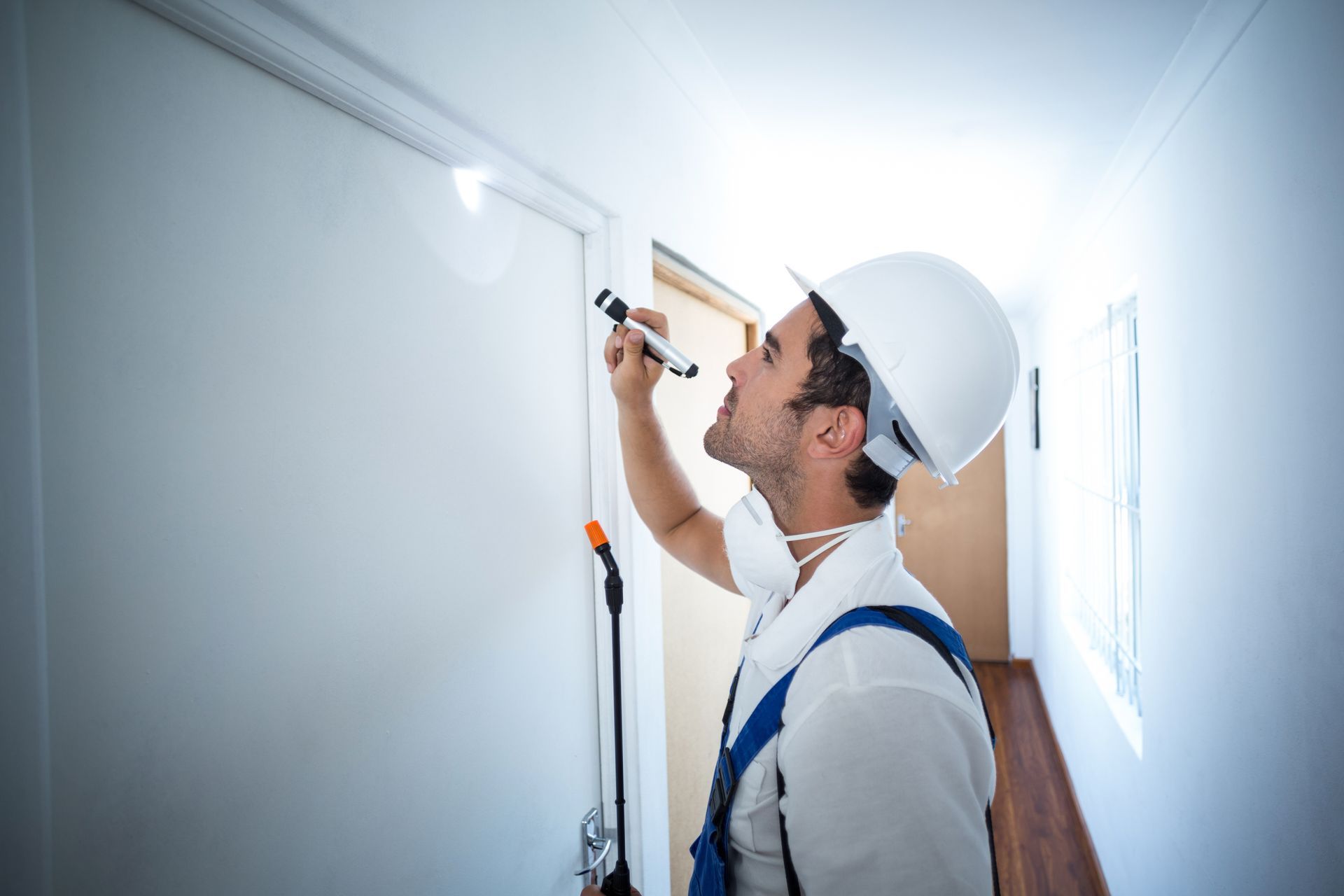 A man in a hard hat is looking at a door with a flashlight.