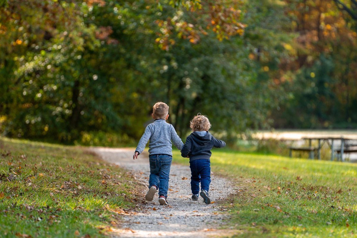 Two children are holding hands and walking down a path