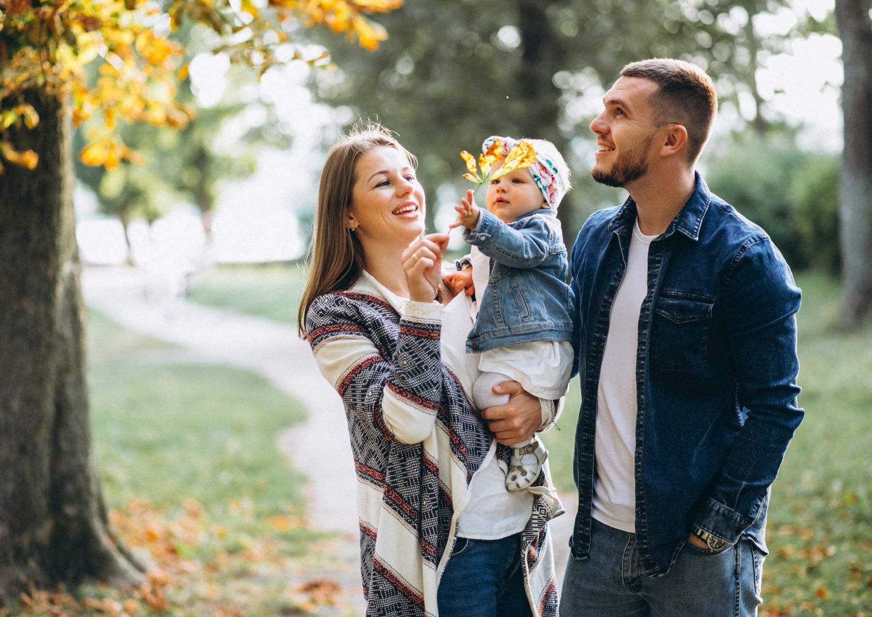 A man and woman are holding a baby in their arms in a park.
