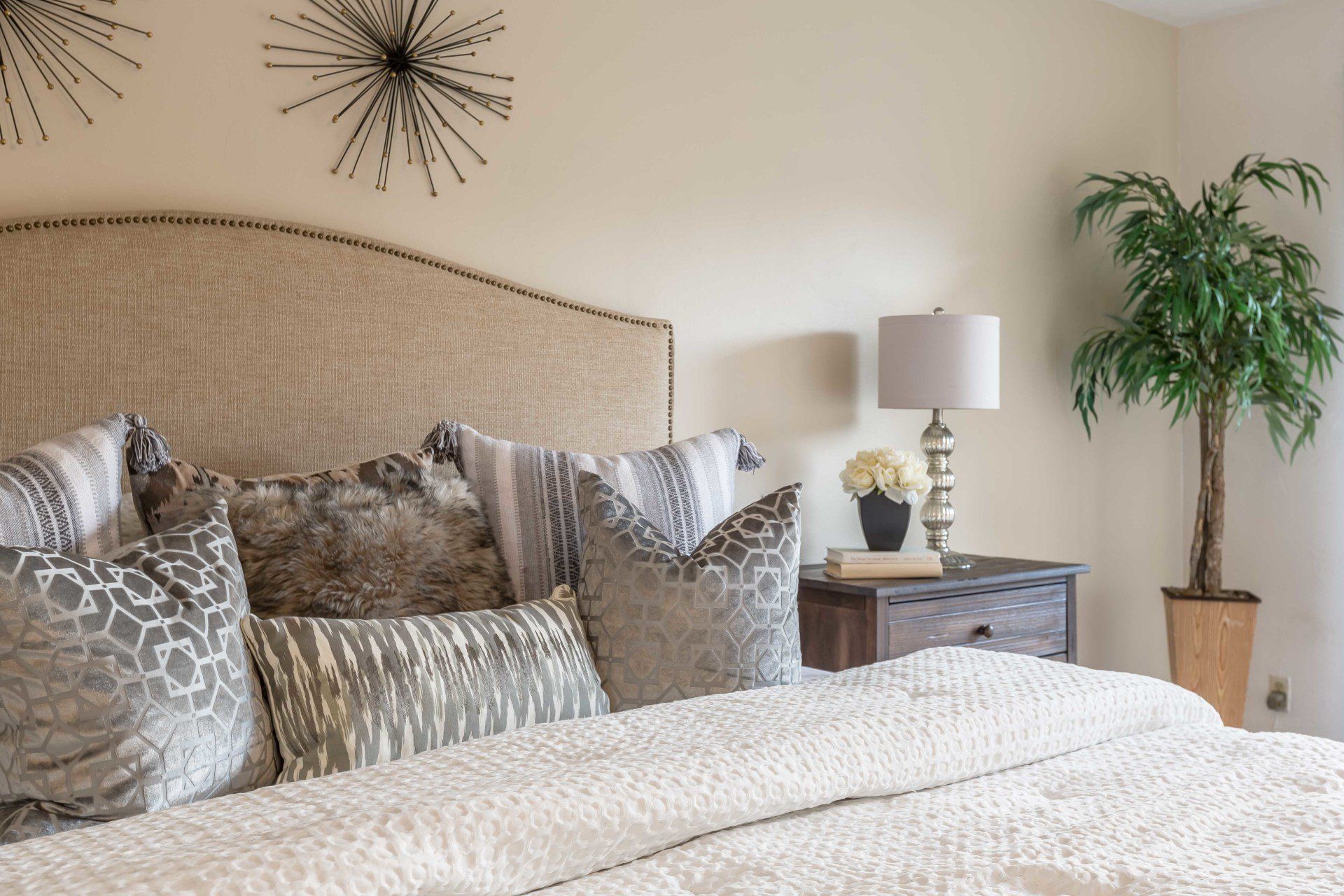 A bedroom with a bed , nightstand , lamp and plant.