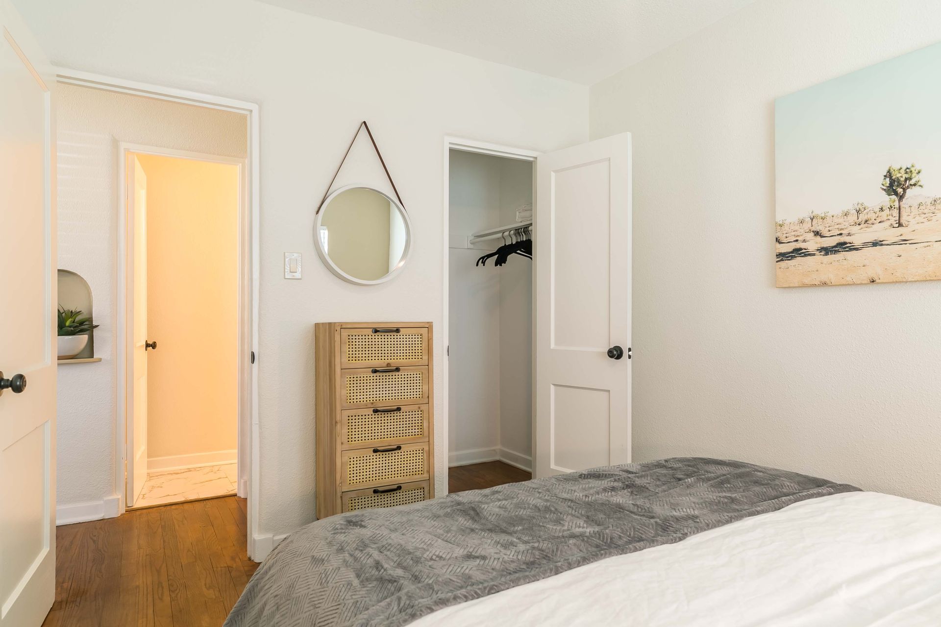 A bedroom with a bed , dresser , mirror and painting on the wall.