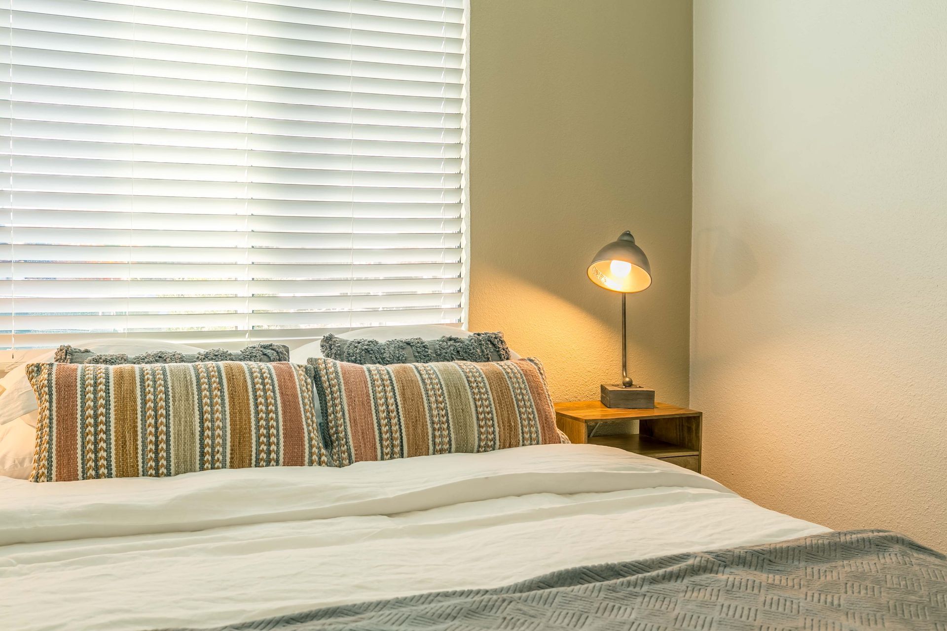 A bedroom with a bed , nightstand , lamp and window.