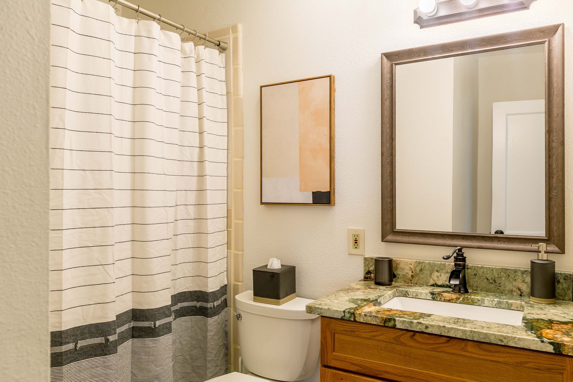 A bathroom with a toilet , sink , mirror and shower curtain.