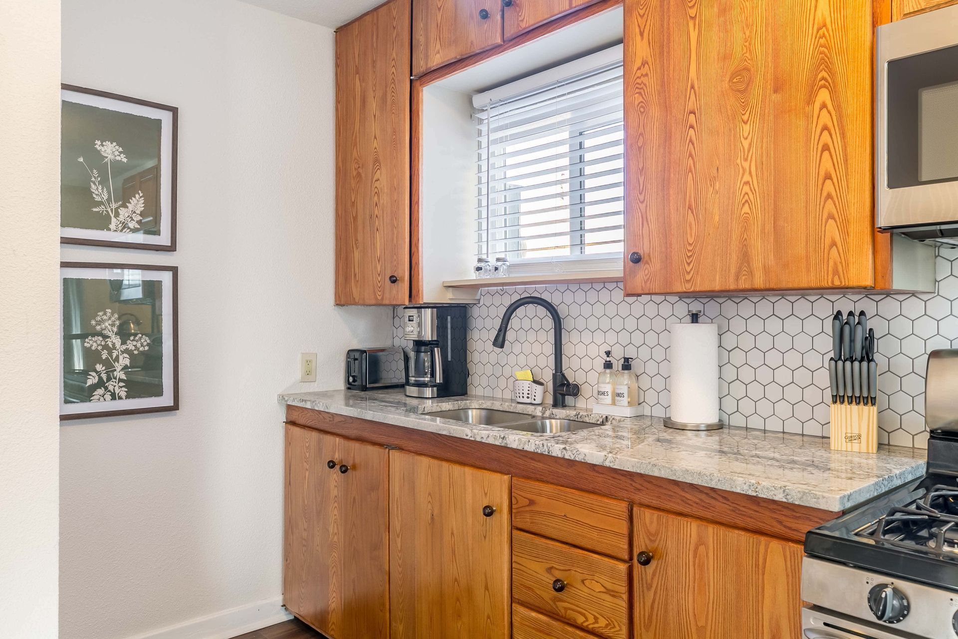 A kitchen with wooden cabinets , granite counter tops , a sink , stove , microwave and a window.