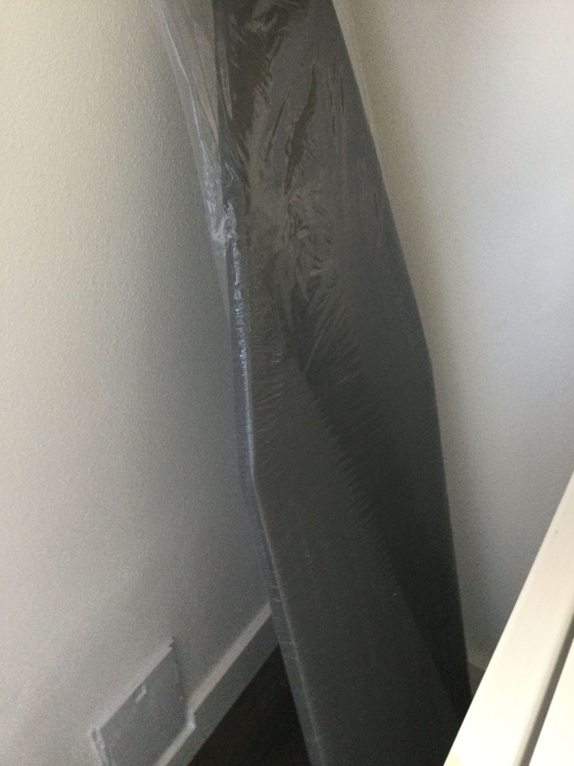 A gray ironing board is sitting next to a white wall.