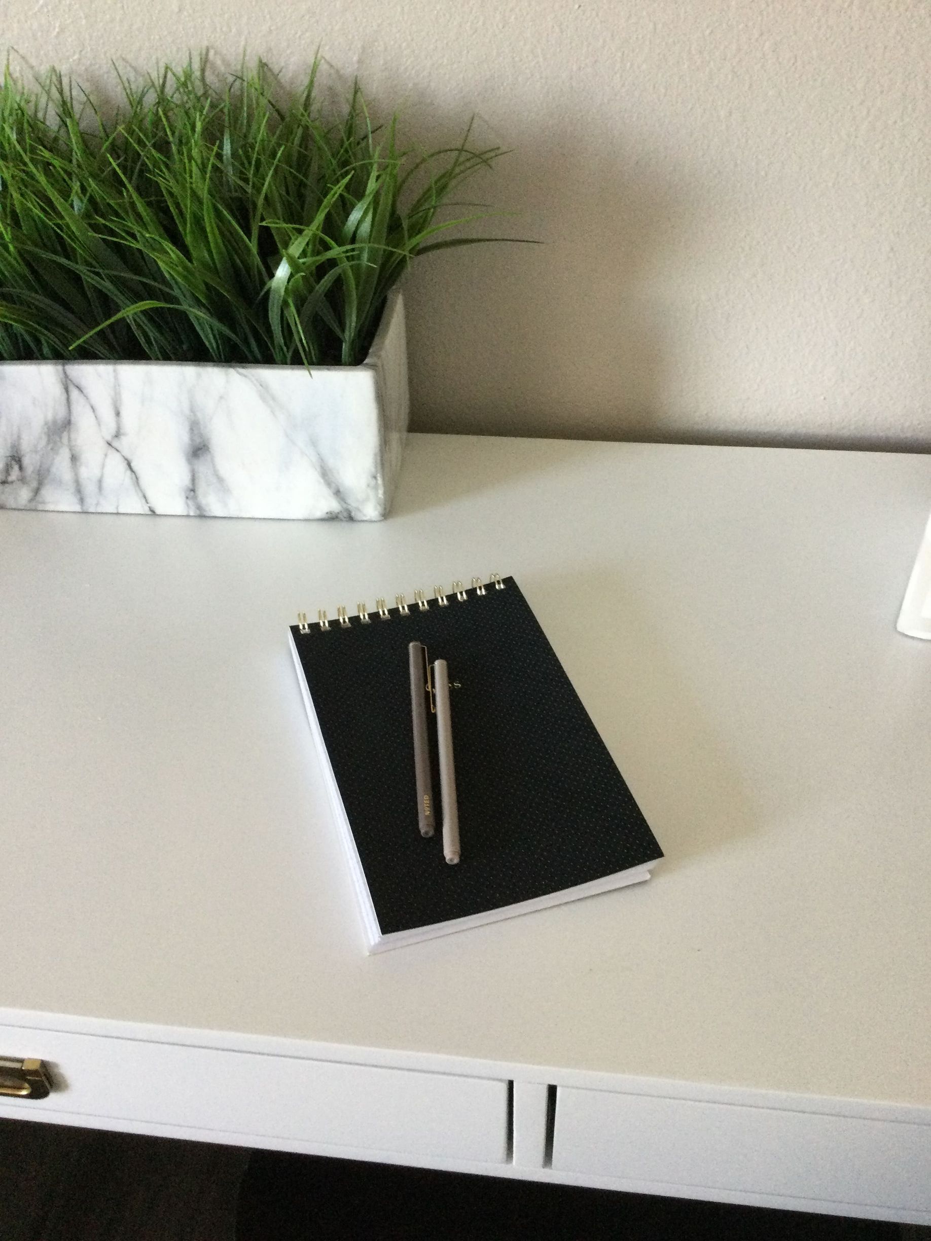 A black notebook and two pens are on a white desk.