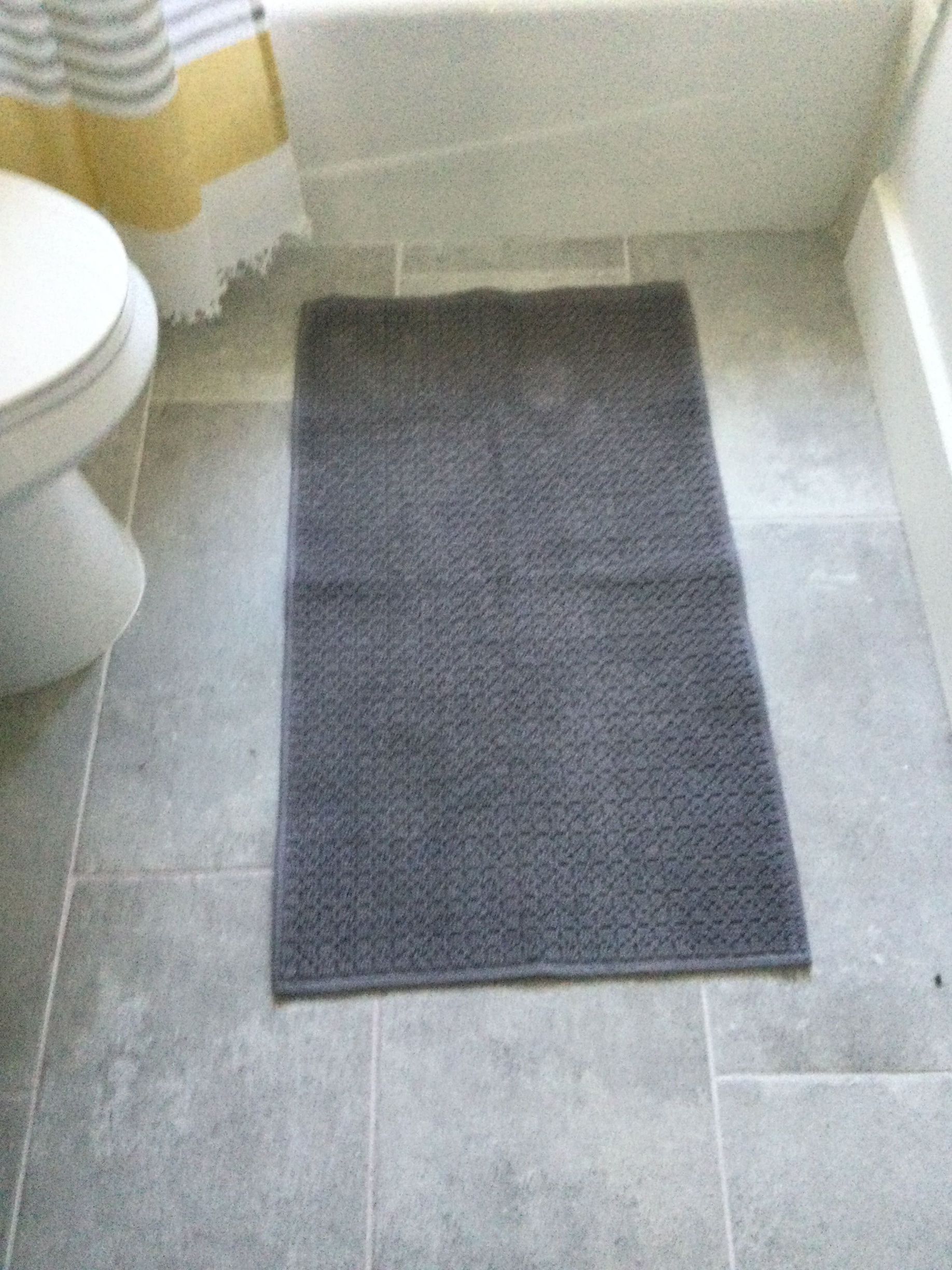 A gray rug is sitting on the floor in a bathroom next to a toilet.