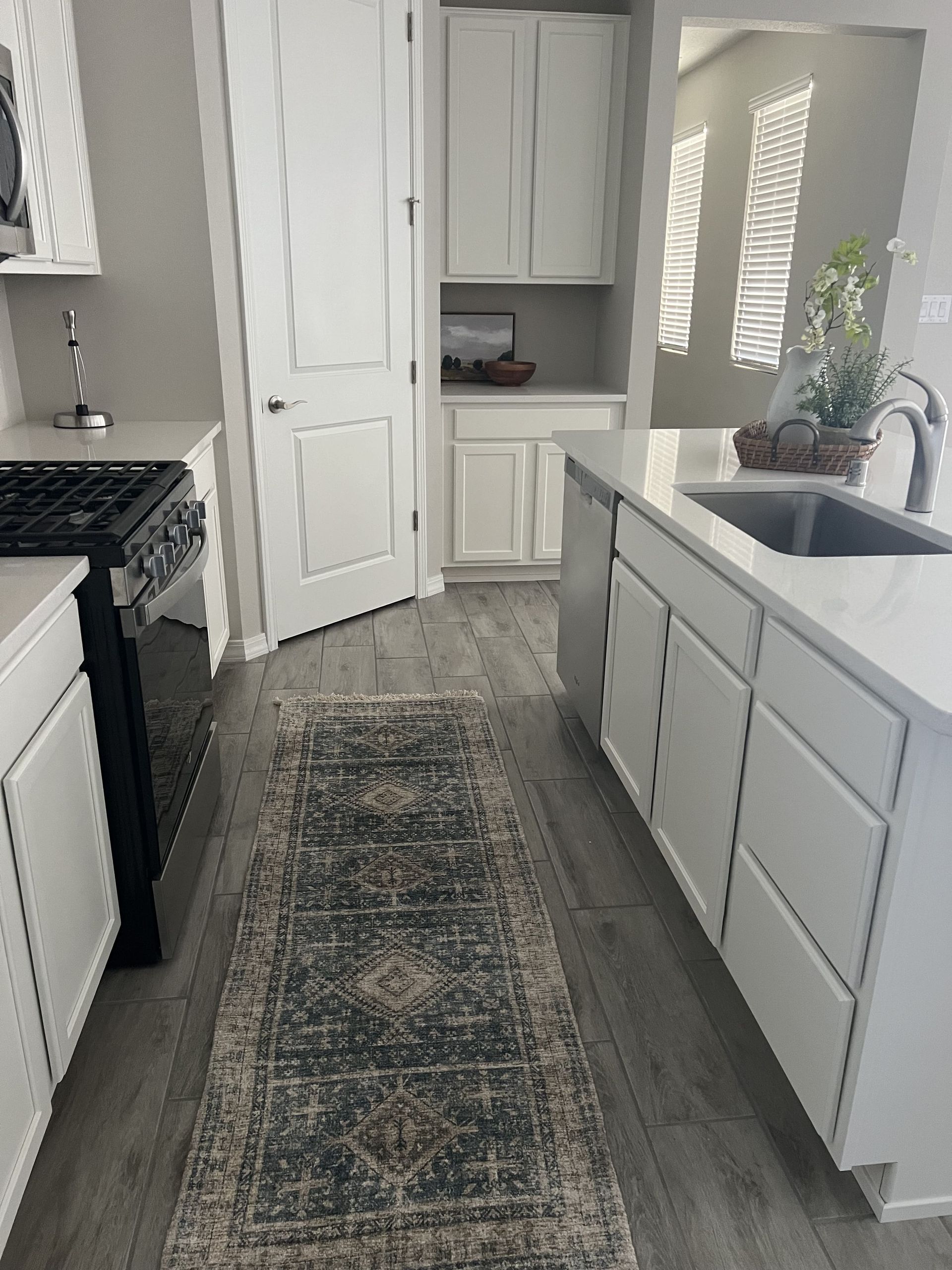 A kitchen with white cabinets , a stove , a sink , and a rug.