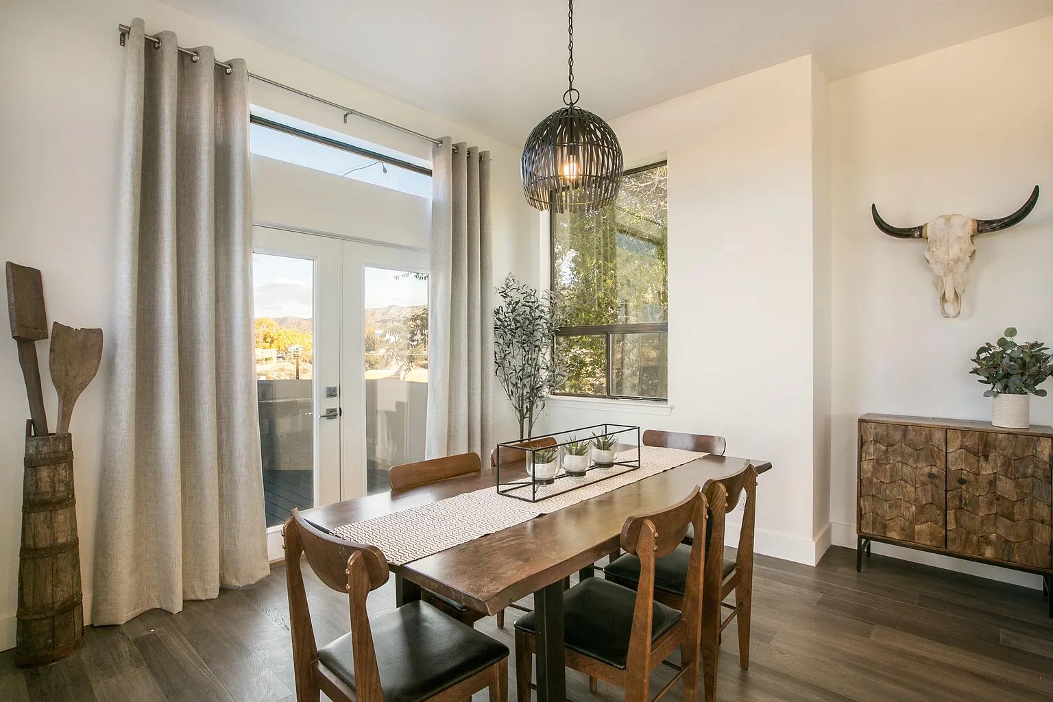 A dining room with a wooden table and chairs and a bull skull on the wall.