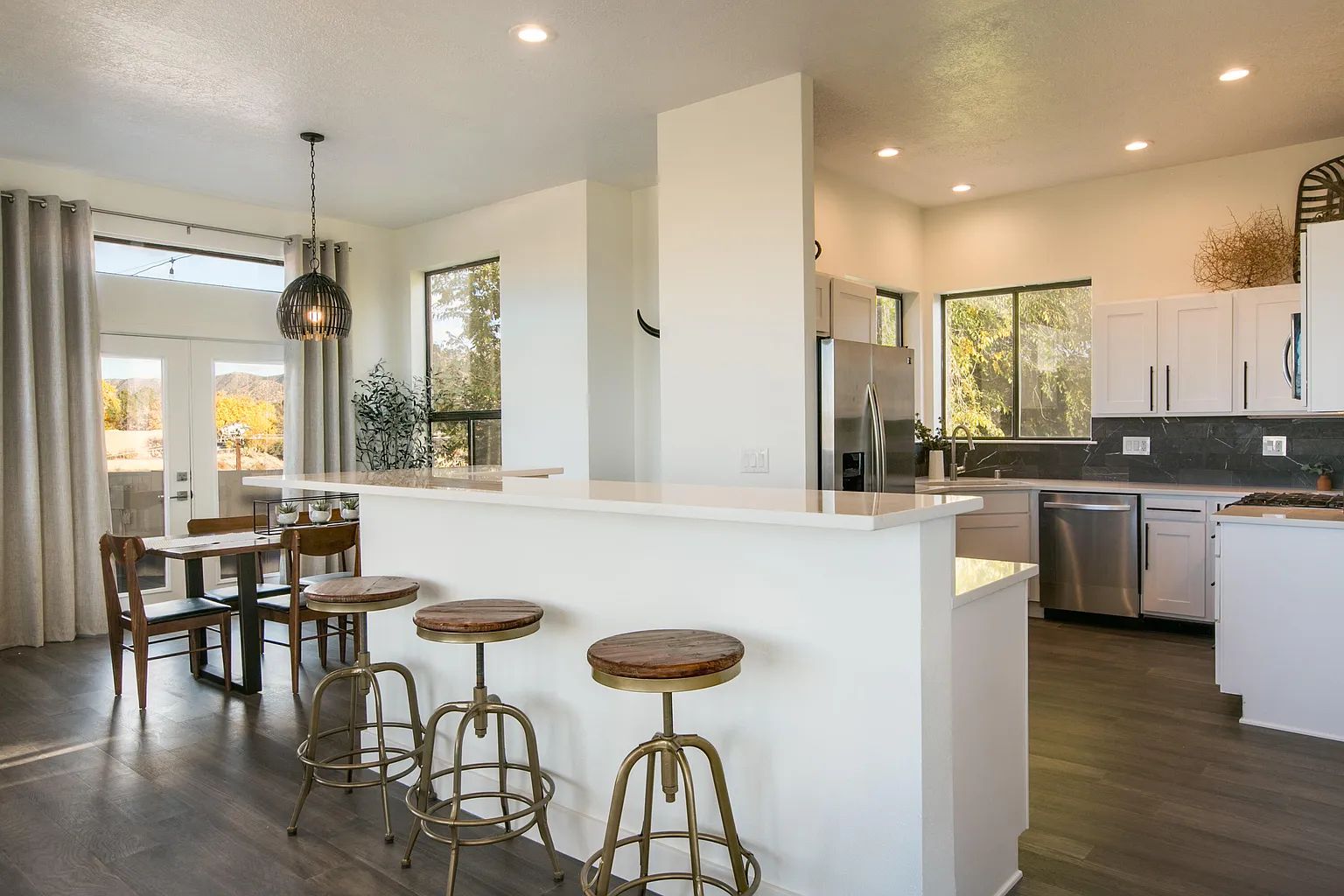 A kitchen with white cabinets , stainless steel appliances , a dining room and a bar.