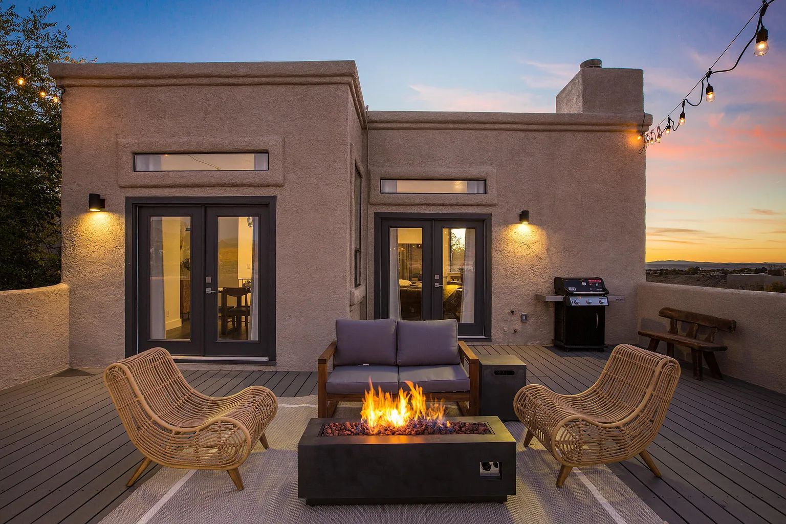 A patio with a fire pit and chairs in front of a house.