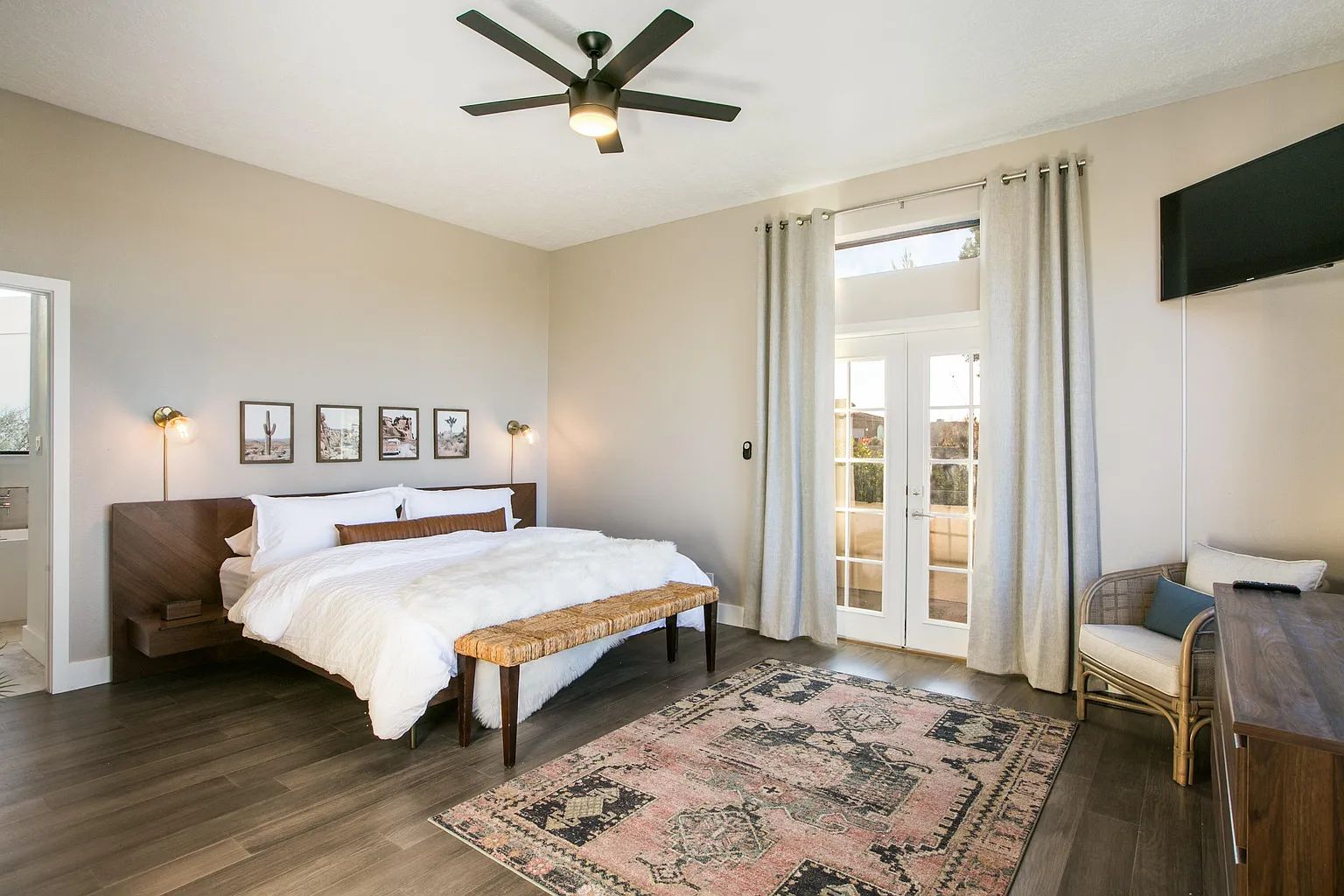 A bedroom with a large bed , a bench , a rug and a ceiling fan.