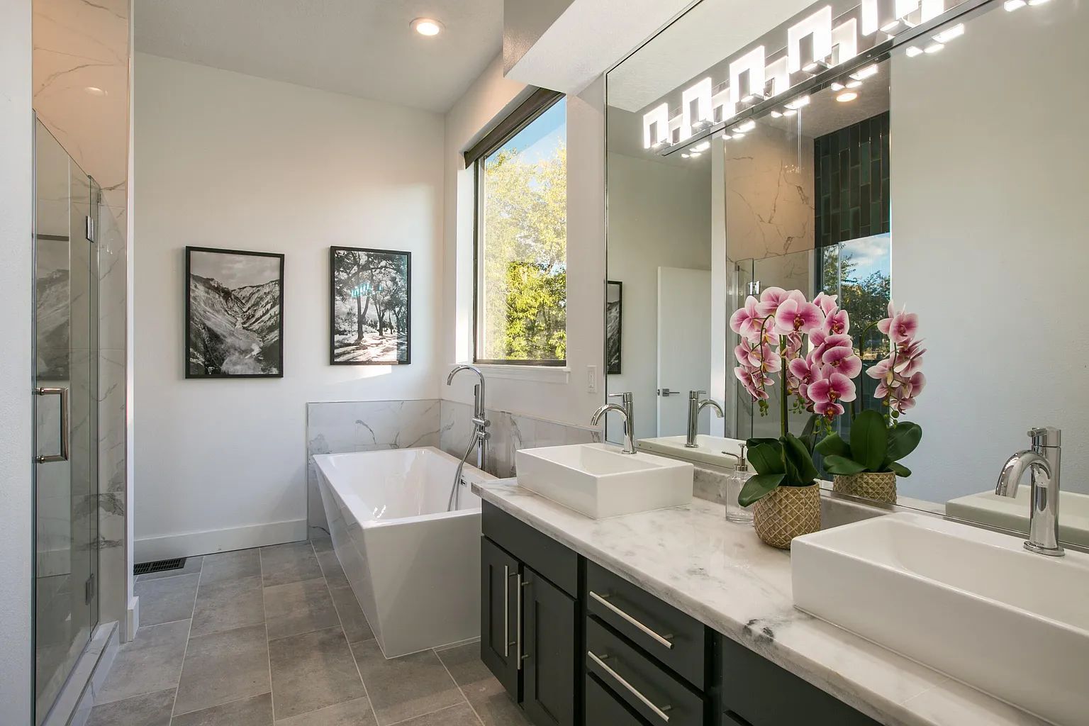 A bathroom with two sinks , a tub , and a large mirror.