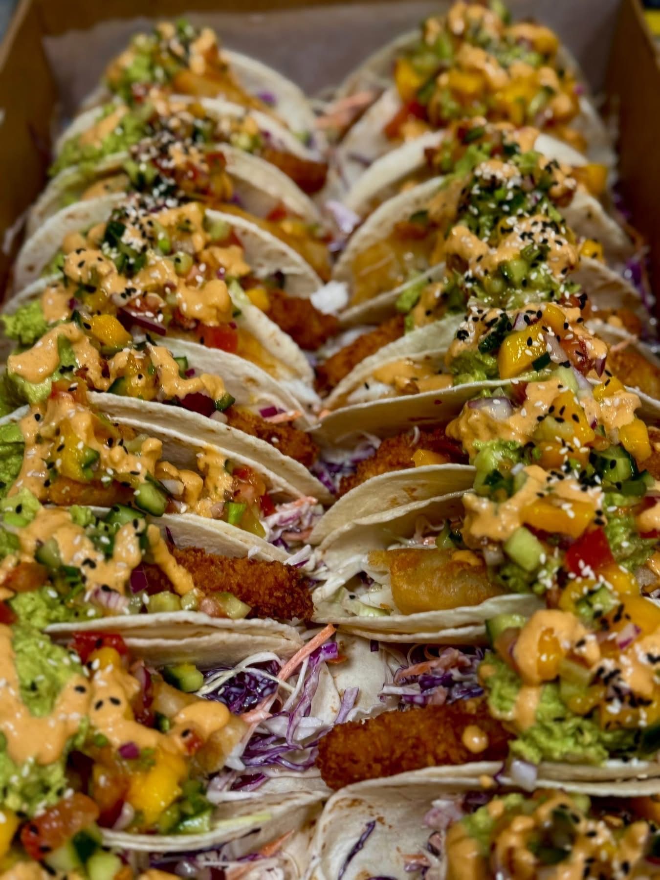Box of colorful fish tacos with mango salsa, avocado, and sauce.