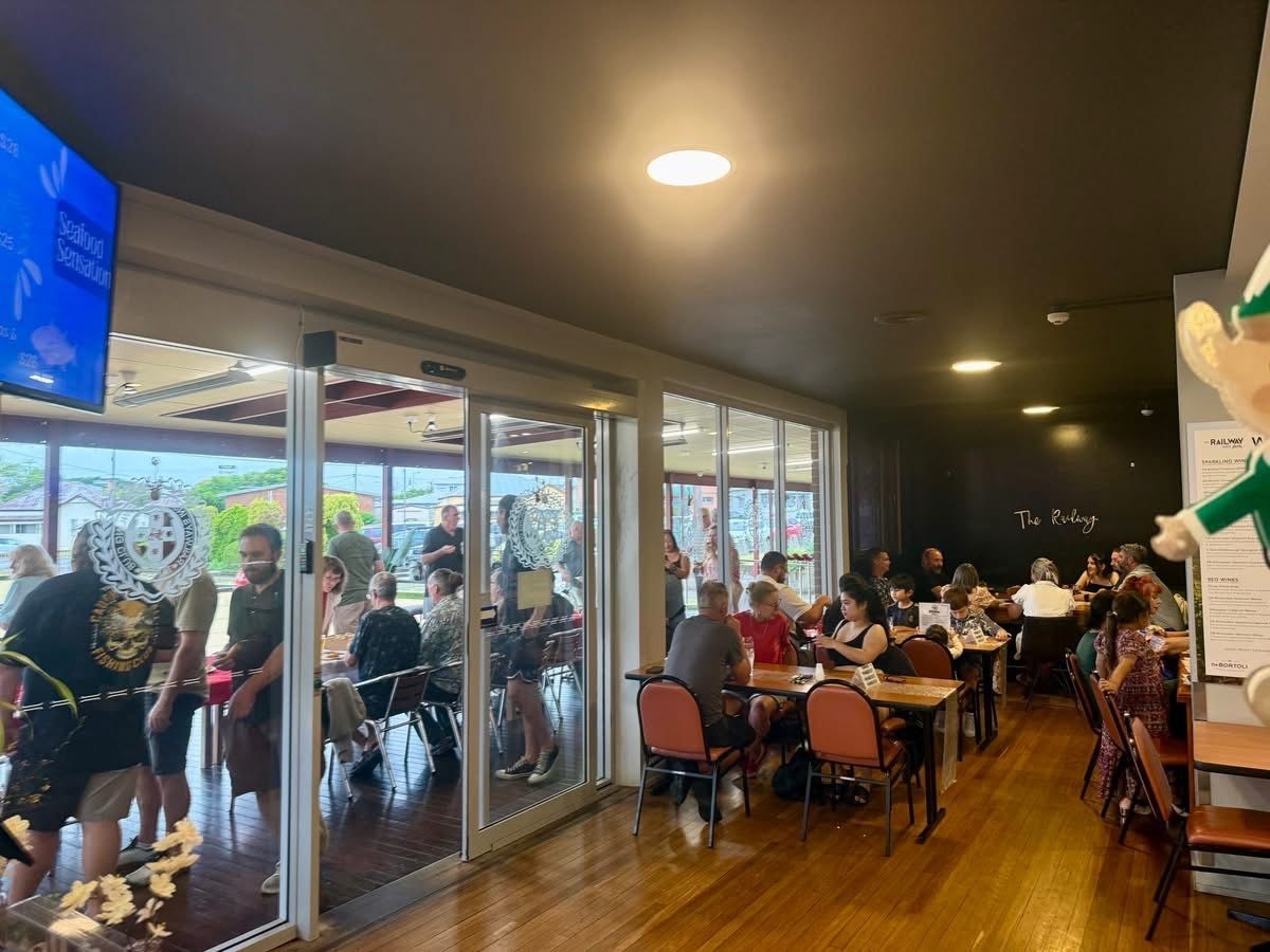 People at tables and standing near an open doorway. Restaurant interior with dark walls and wooden floors.