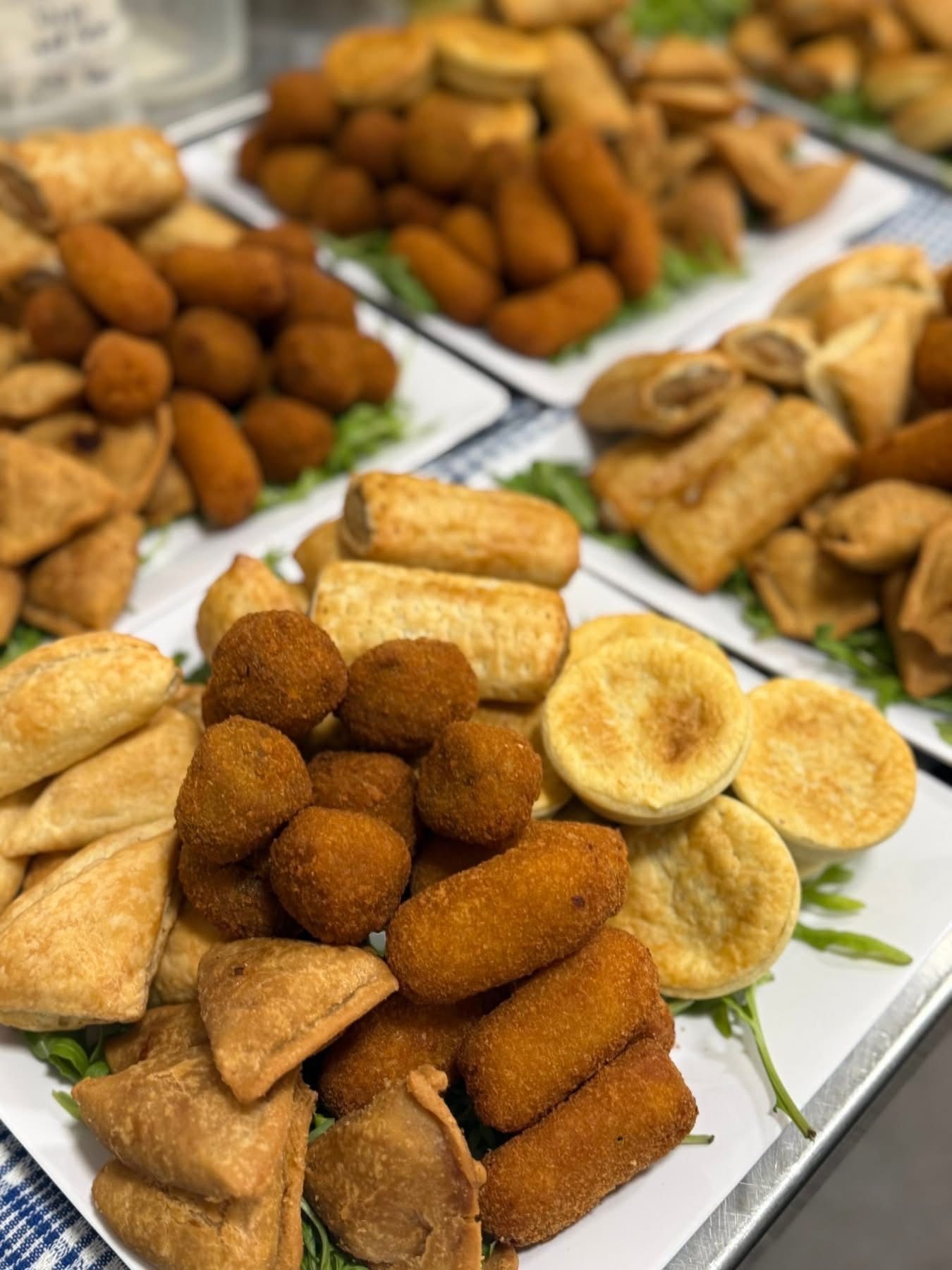 Platters of assorted fried appetizers, including croquettes, pies, and pastries, arranged on green garnish.