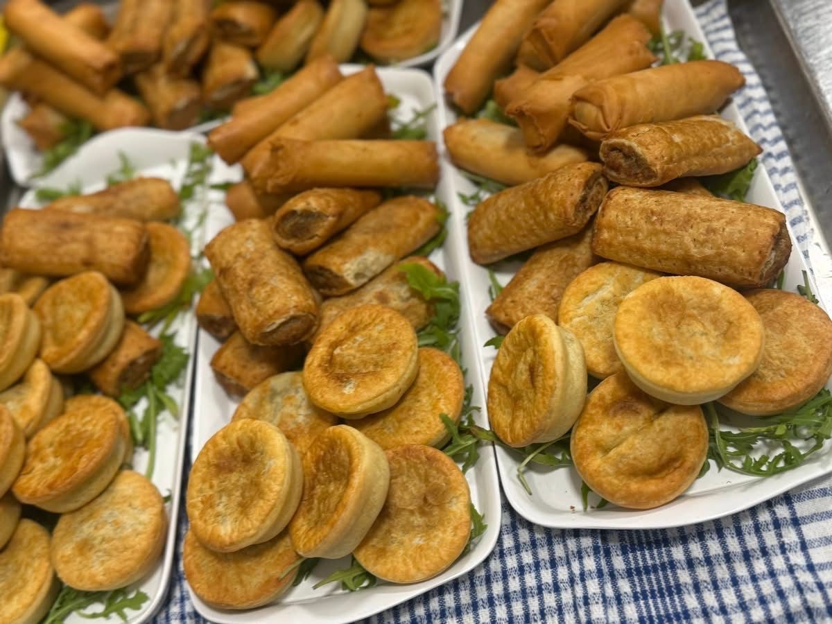 Trays of assorted savory pastries: sausage rolls, mini pies, and spring rolls.