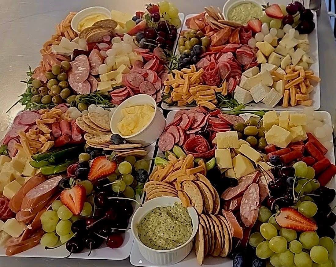 Charcuterie boards with various cheeses, meats, fruits, olives, crackers, and dips arranged on white platters.