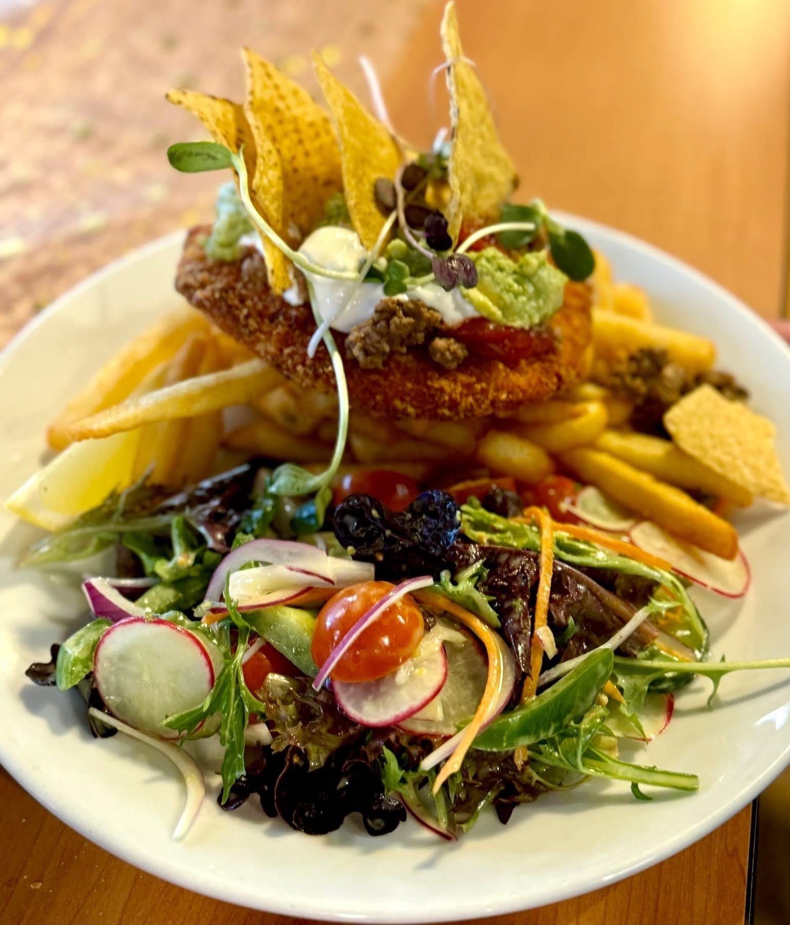 Plate with a breaded fried chicken breast, fries, salad, and toppings: guacamole, sour cream, chips.