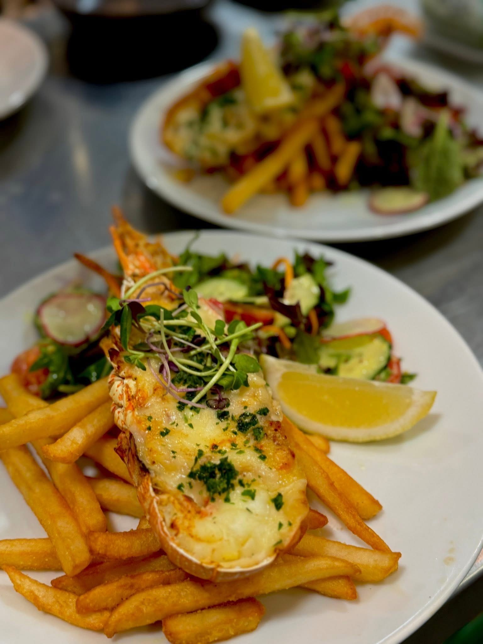 Lobster thermidor with fries, salad, and lemon wedge on a white plate.
