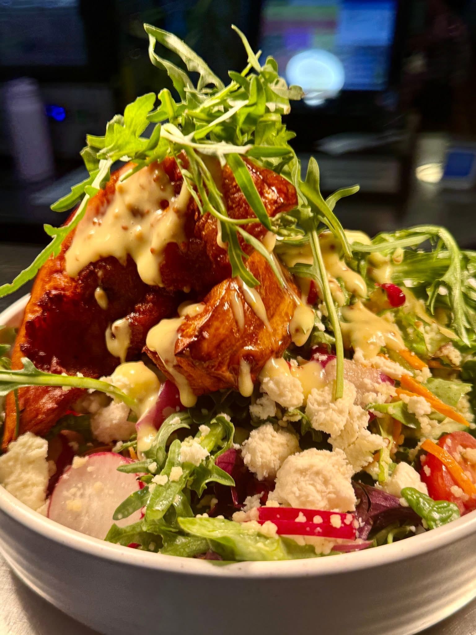 Salad bowl with fried, glazed chicken, arugula, feta, vegetables and dressing.