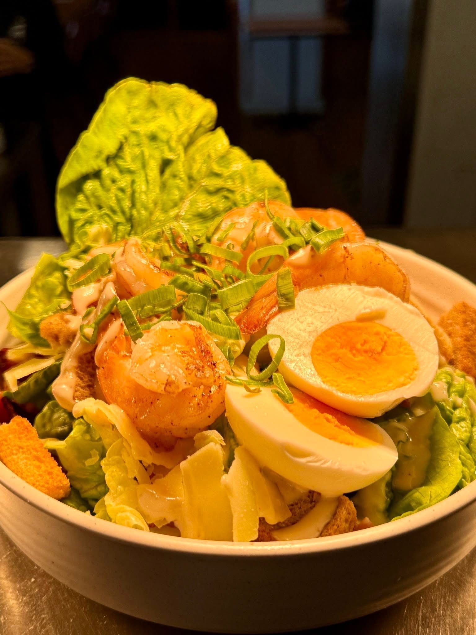 Shrimp Caesar salad in a white bowl: romaine lettuce, croutons, egg, and green onions.