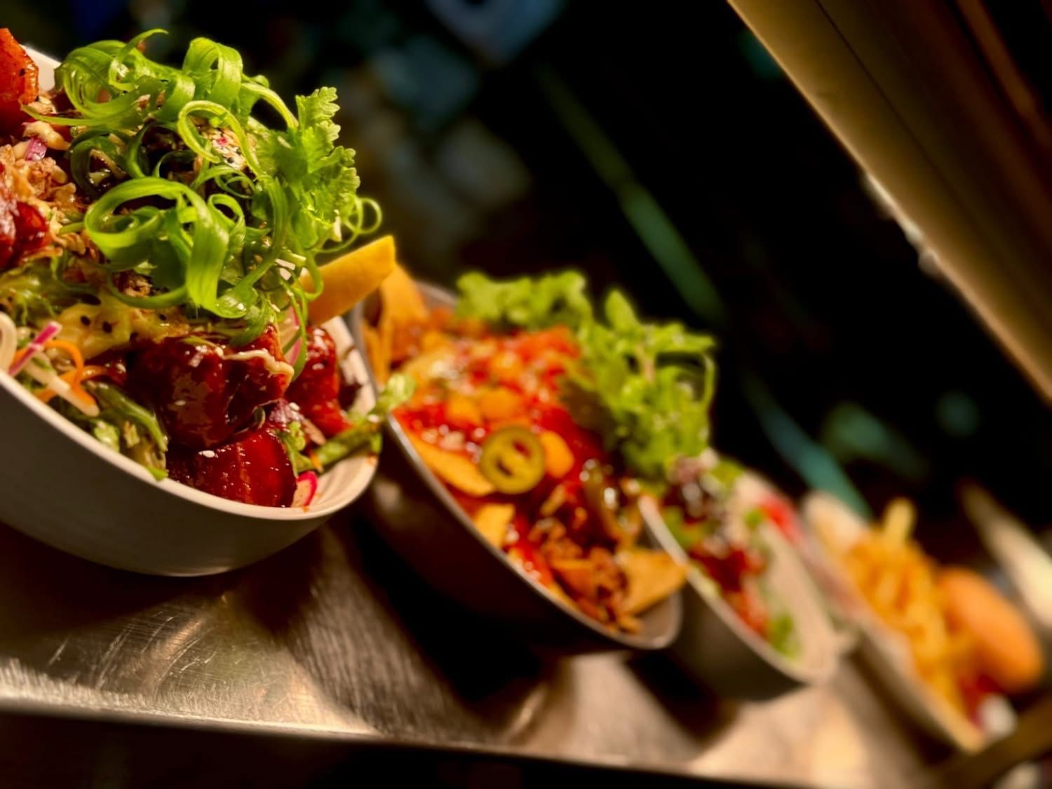 Bowls of nachos, salads, and fries on a counter, garnished with green onions, lettuce, and jalapeños.