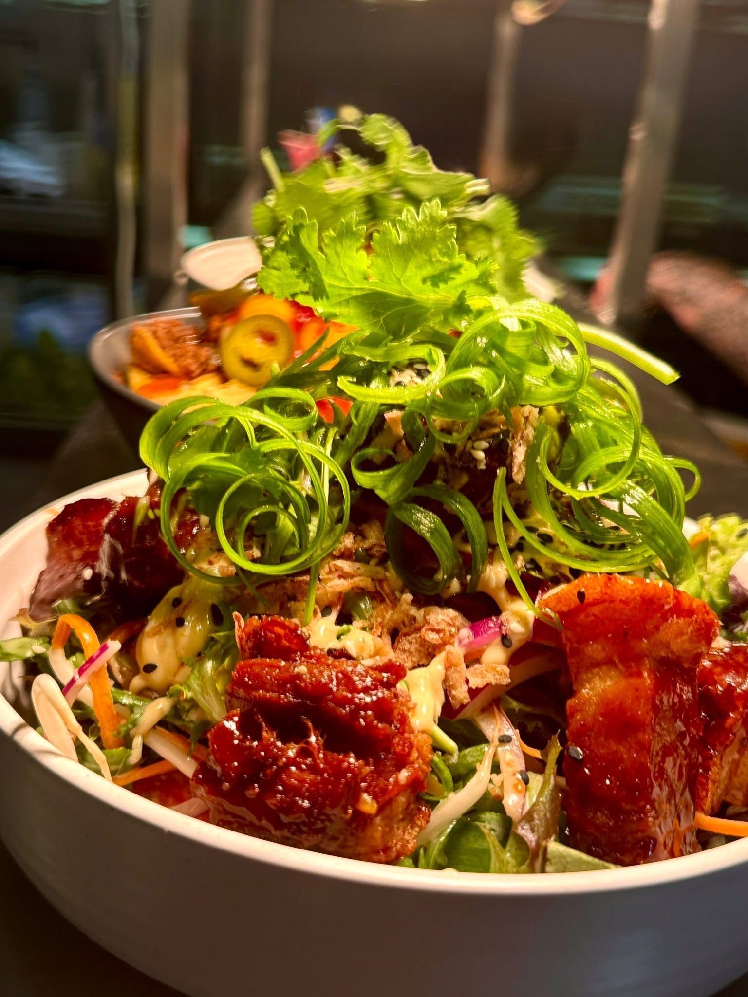 Bowl of colorful salad with crispy pork belly and green garnish.