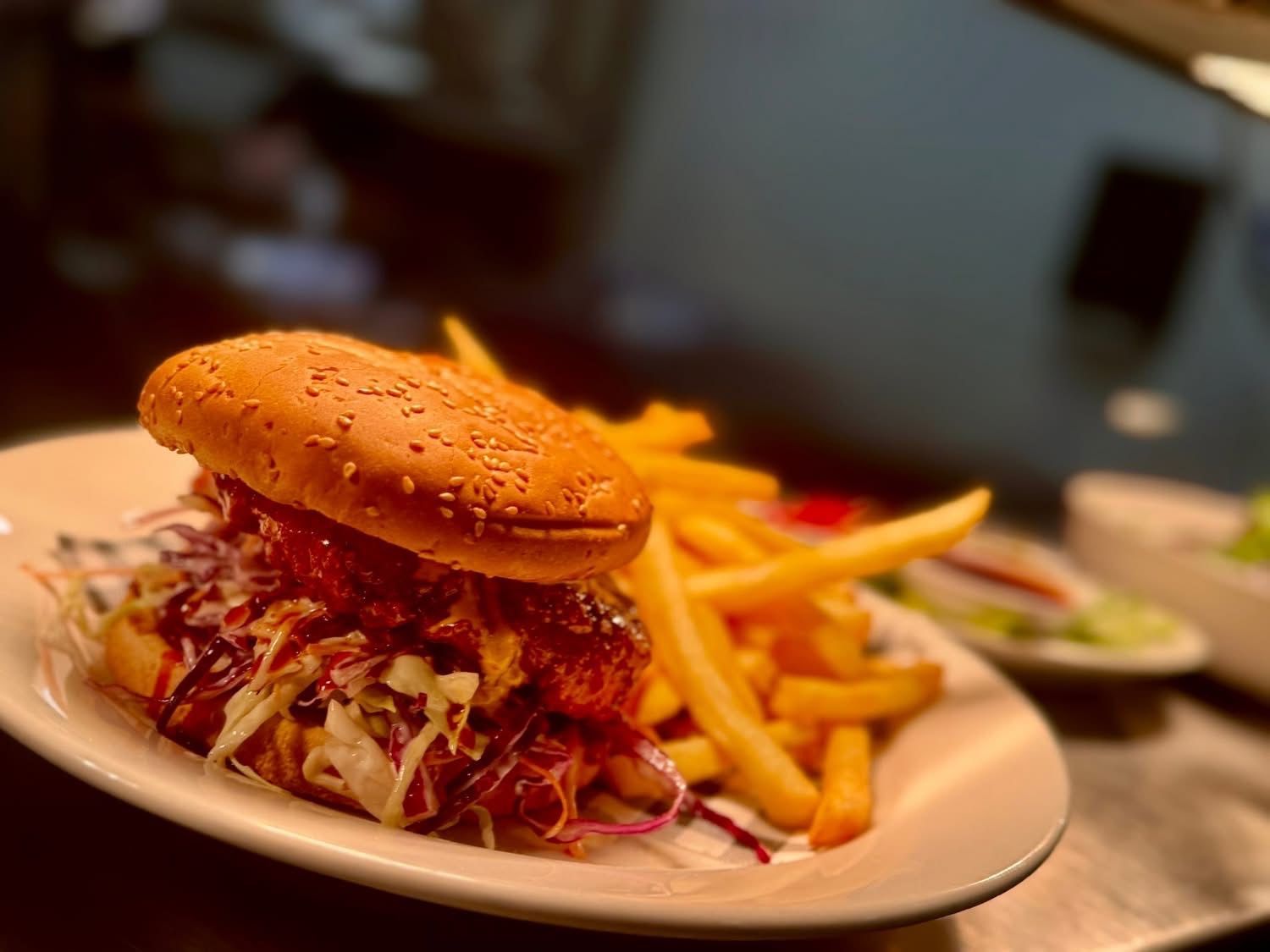 Burger with fries on a plate. The burger has coleslaw and sauce. Golden fries sit beside it.