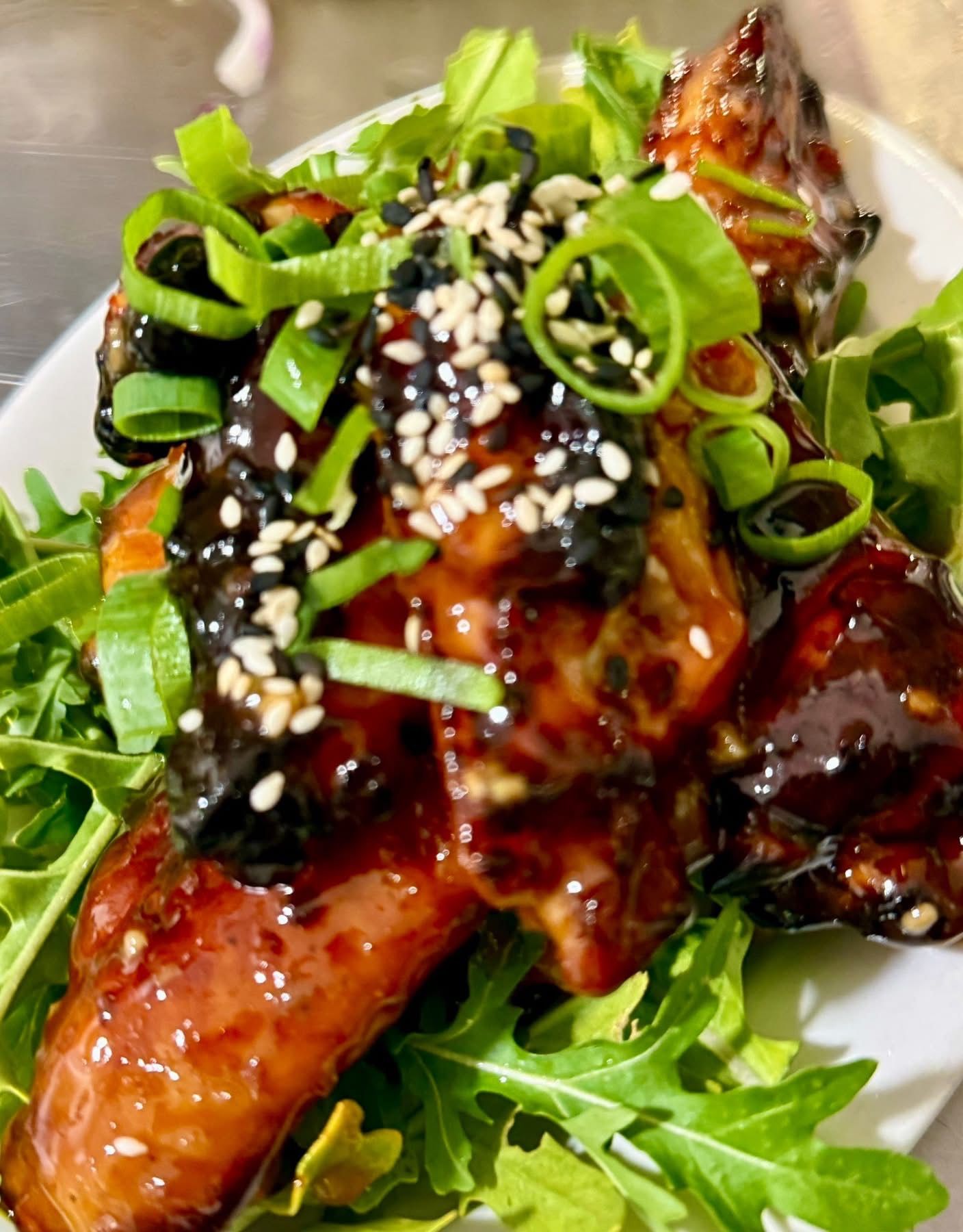 Glazed chicken wings with sesame seeds and scallions, served on a bed of greens.