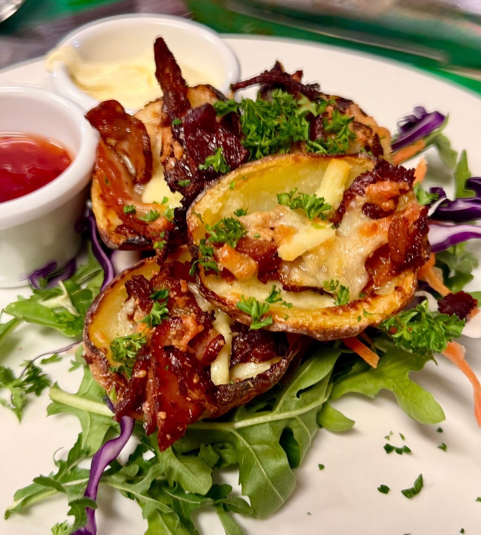 Potato skins topped with bacon and cheese, served with ketchup and aioli on a bed of greens.