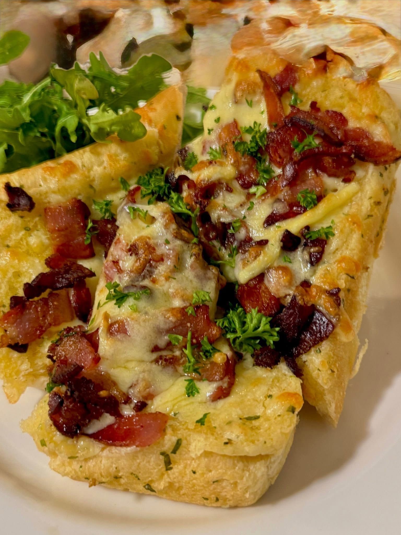 Toasted bread topped with cheese and bacon, garnished with parsley and lettuce.