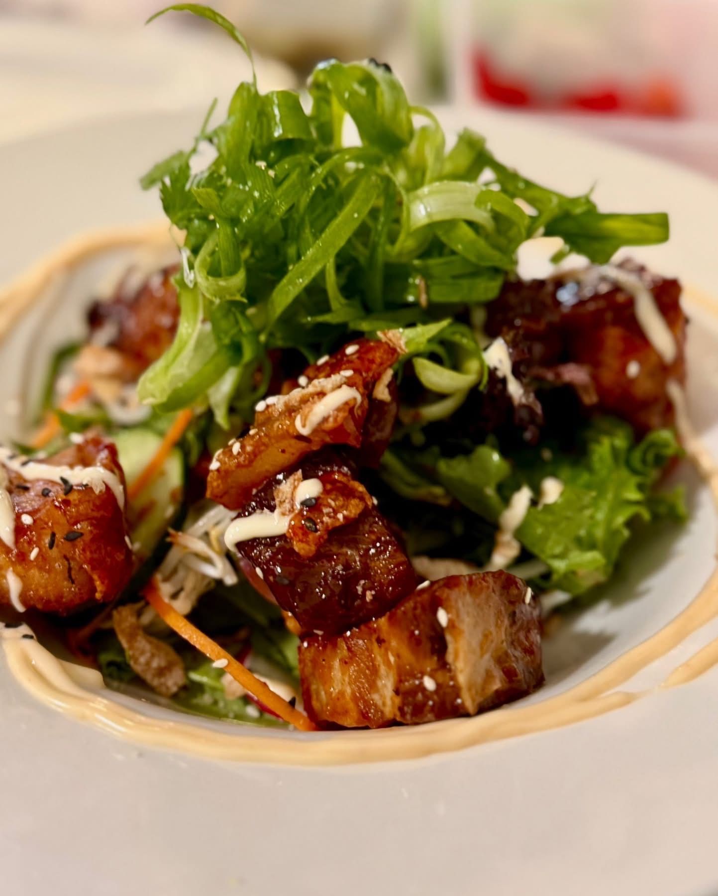 Pork belly salad with sesame seeds, scallions, and a creamy sauce, in a shallow bowl.