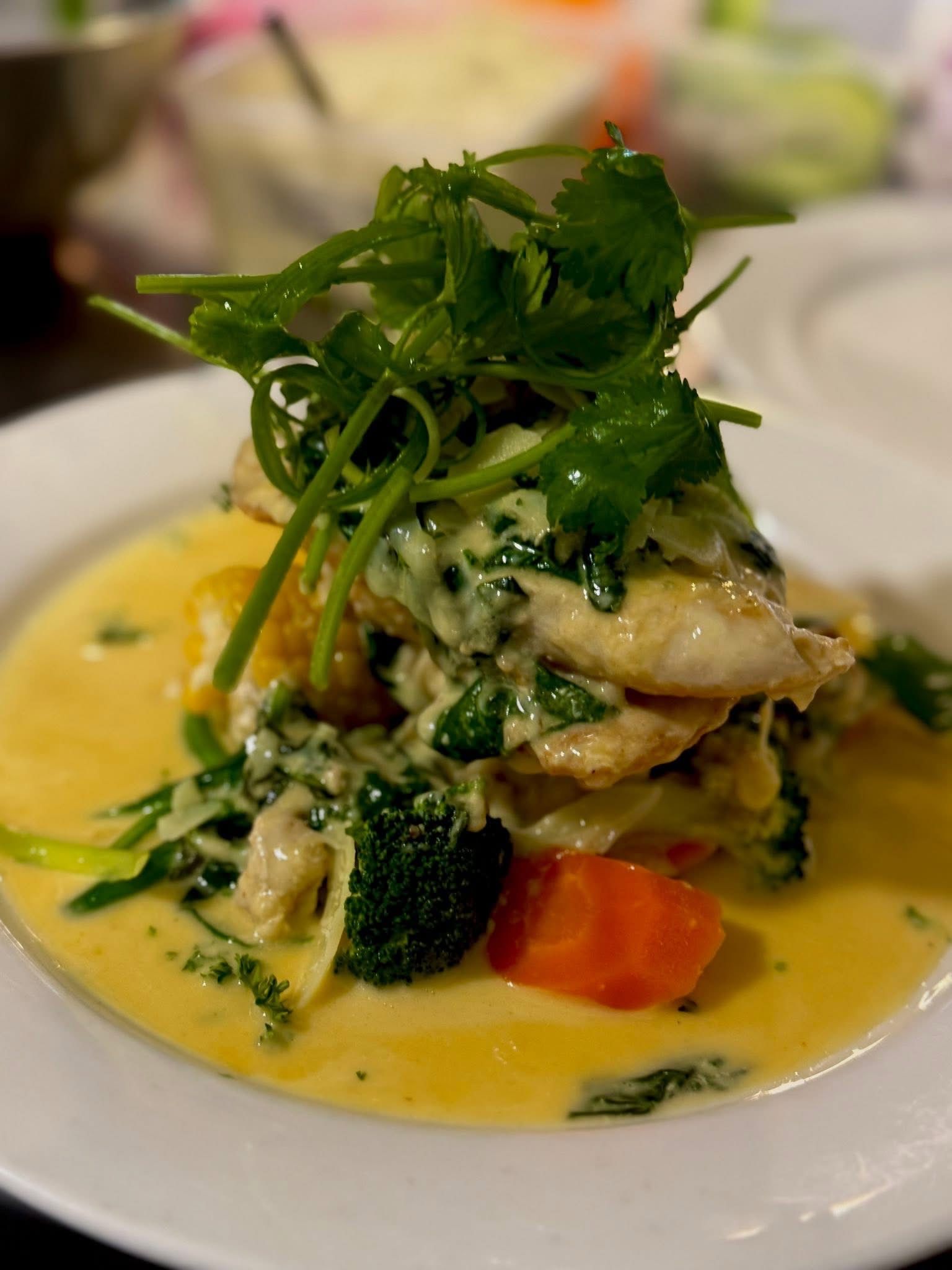Fish and vegetables in yellow sauce, topped with cilantro on a white plate.