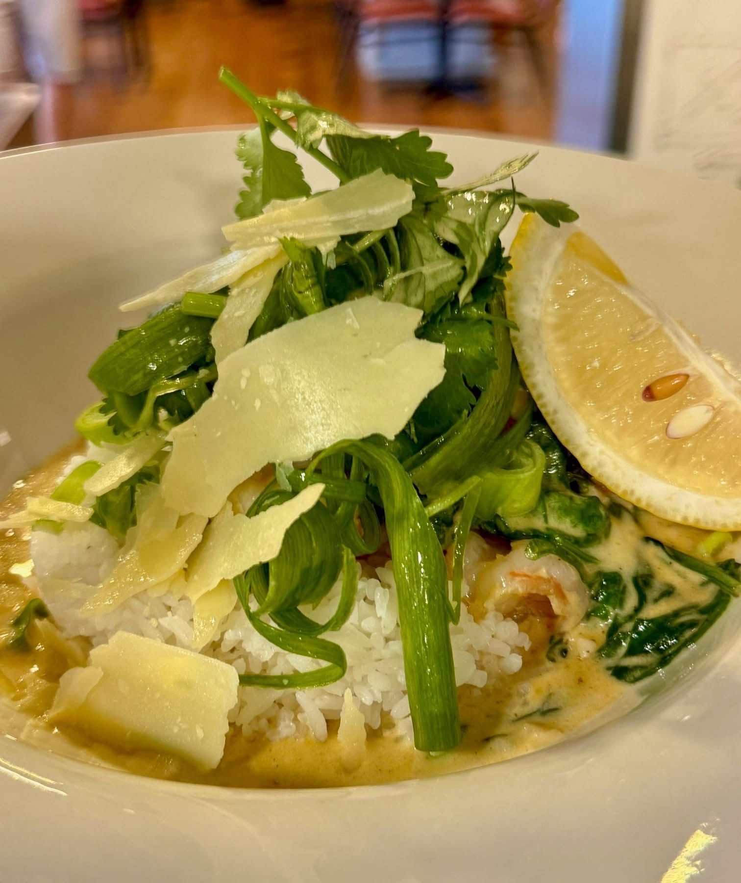 Plate of rice topped with greens, cheese, and a lemon slice. Creamy sauce visible.