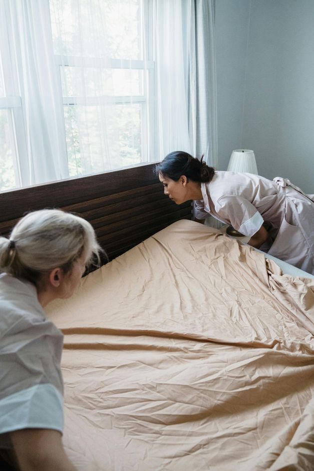 Twee vrouwen maken een bed op in een slaapkamer.