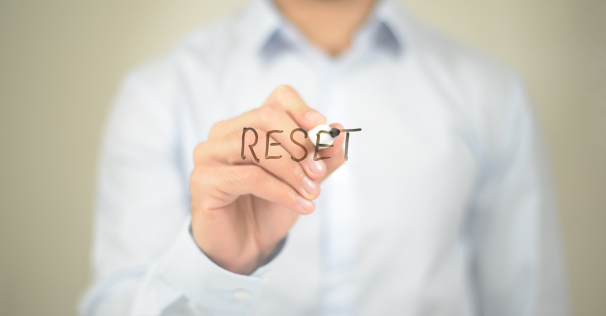 A man is writing the word reset on a screen with a marker.